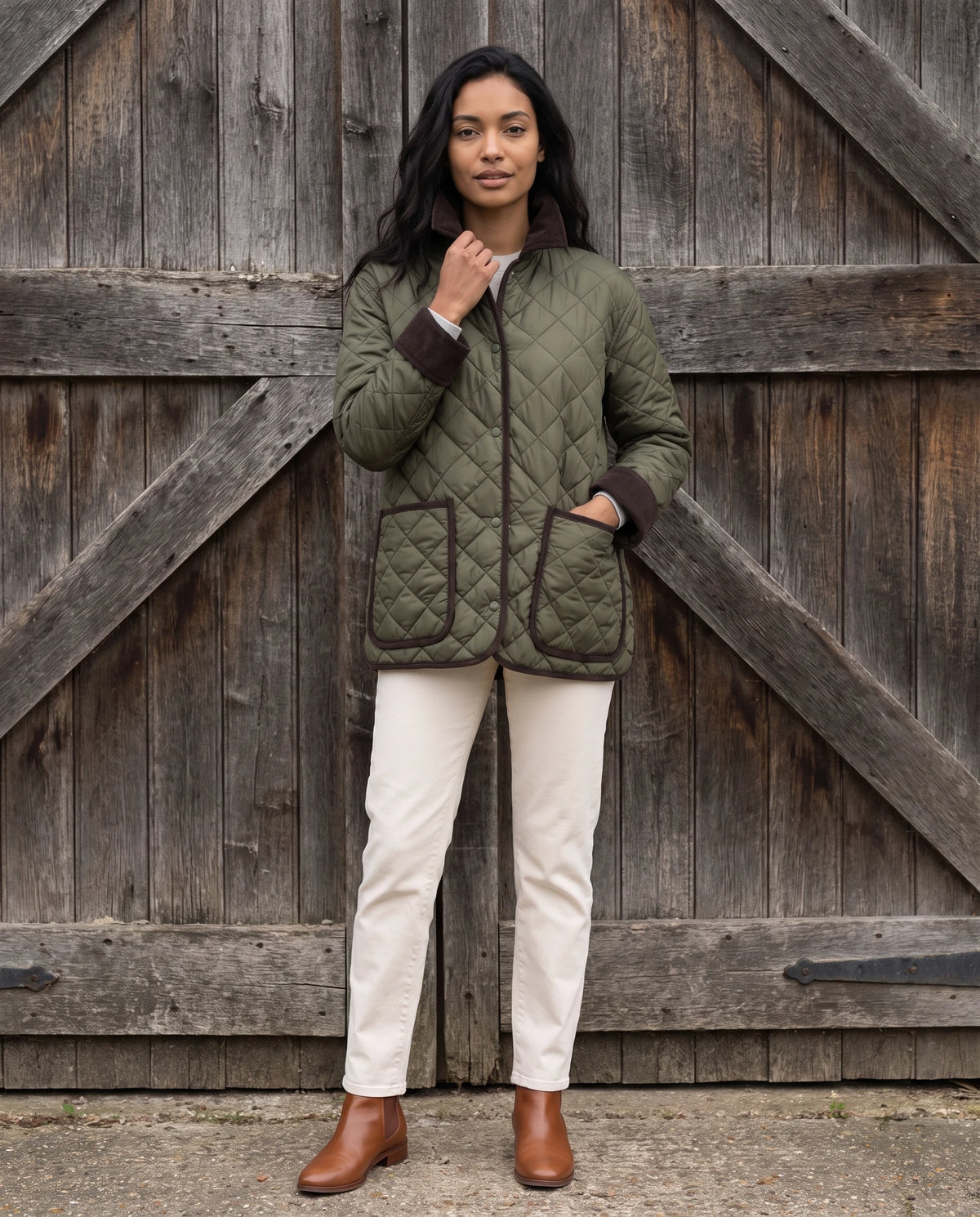 Veste matelassée à col velours côtelé Talia en Vert Olive, portée devant la porte de bois d'une grange, col relevé