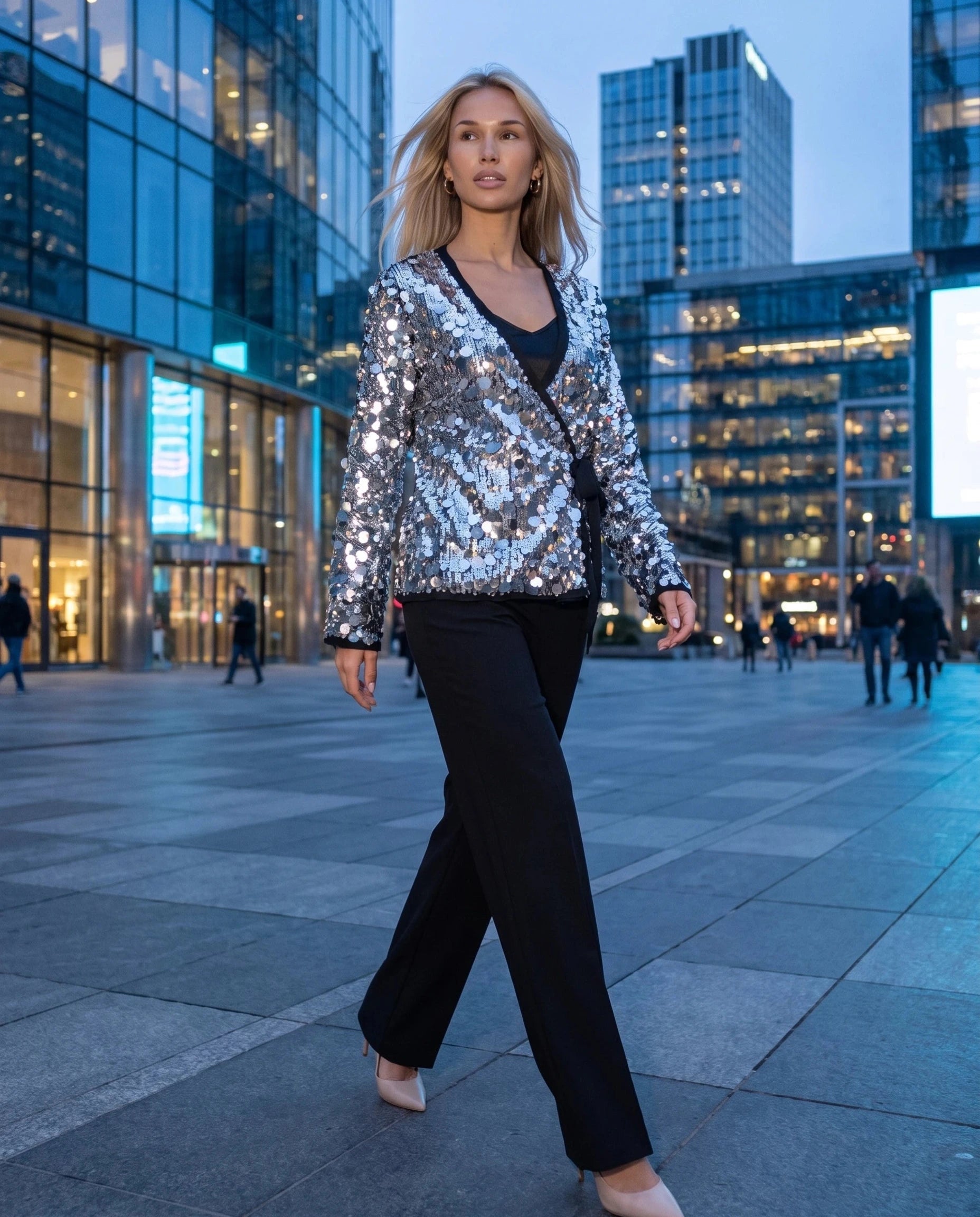 Veste à paillettes argentée Félicie, portée sur une esplanade urbaine à l'heure bleue