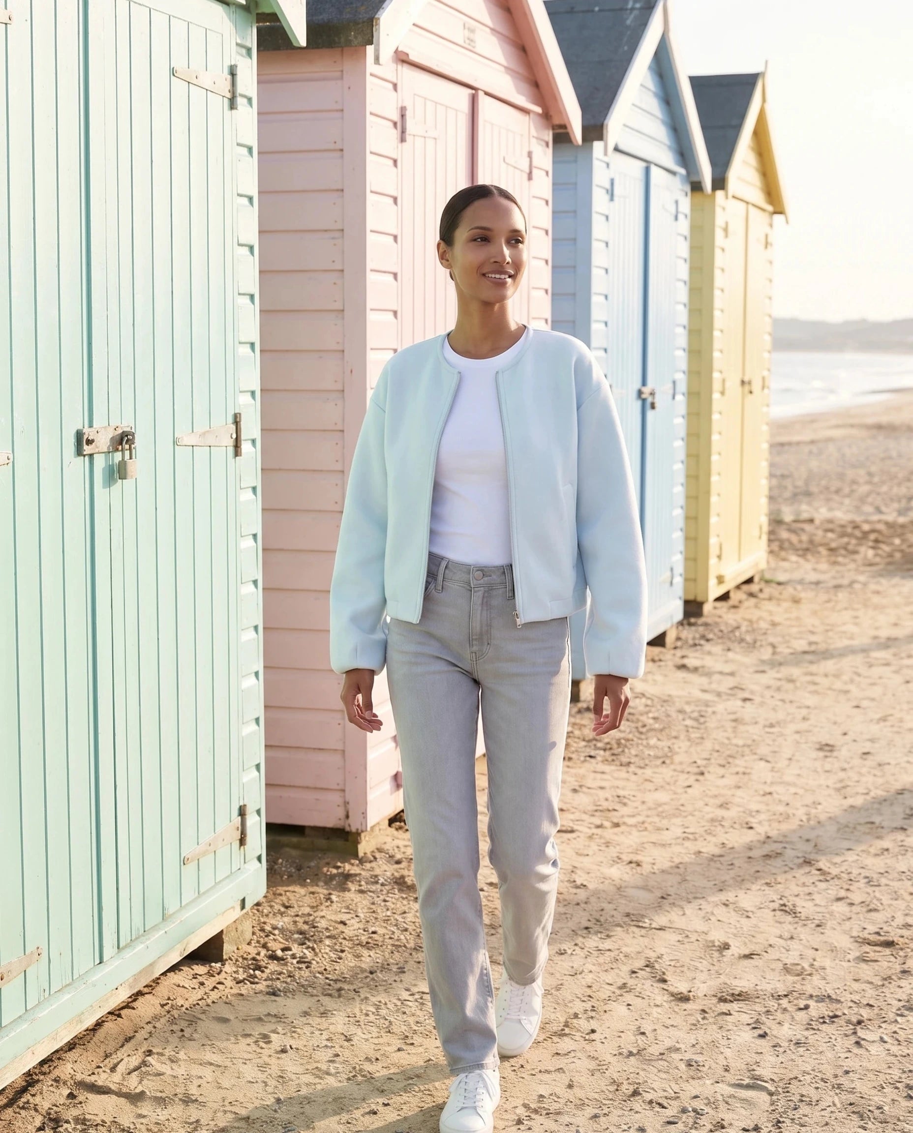 Veste zippée sans col bleu glacier Germaine, portée devant des cabines de plage pastel