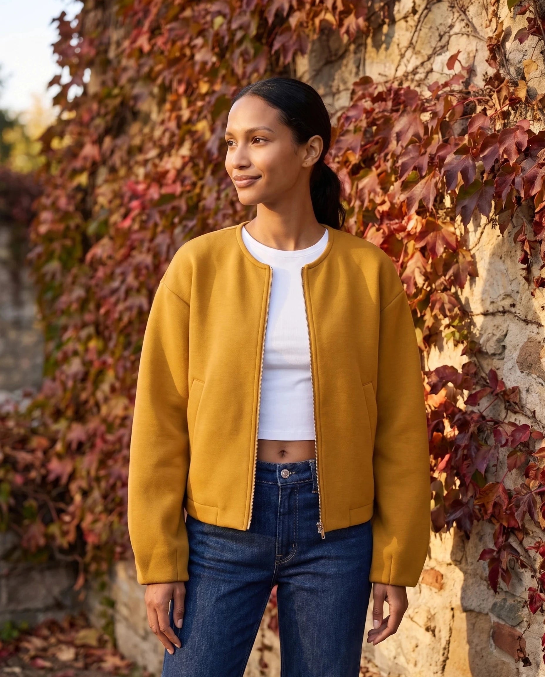Veste zippée sans col jaune moutarde Germaine, portée devant un mur de vigne vierge rousse