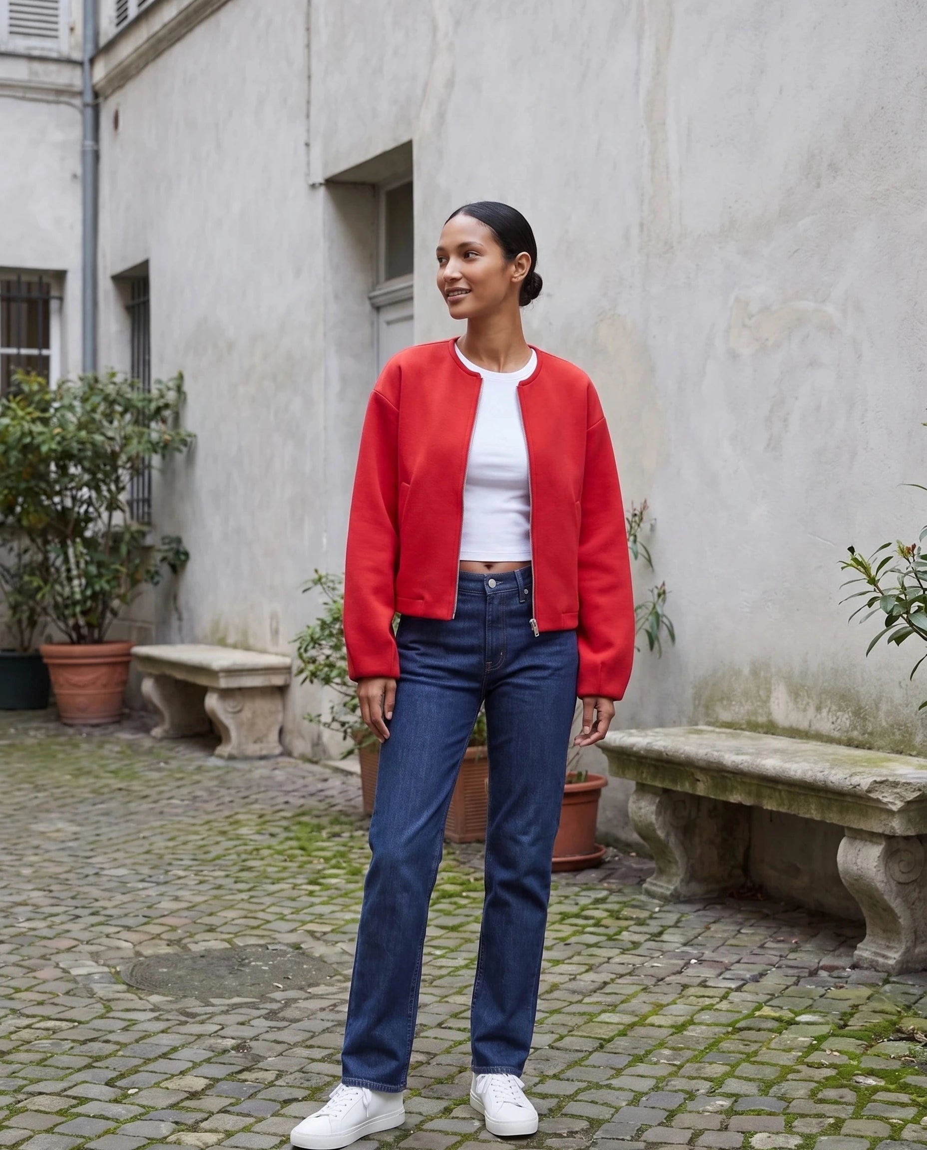 Veste zippée sans col rouge Germaine, portée dans une cour aux murs gris perle
