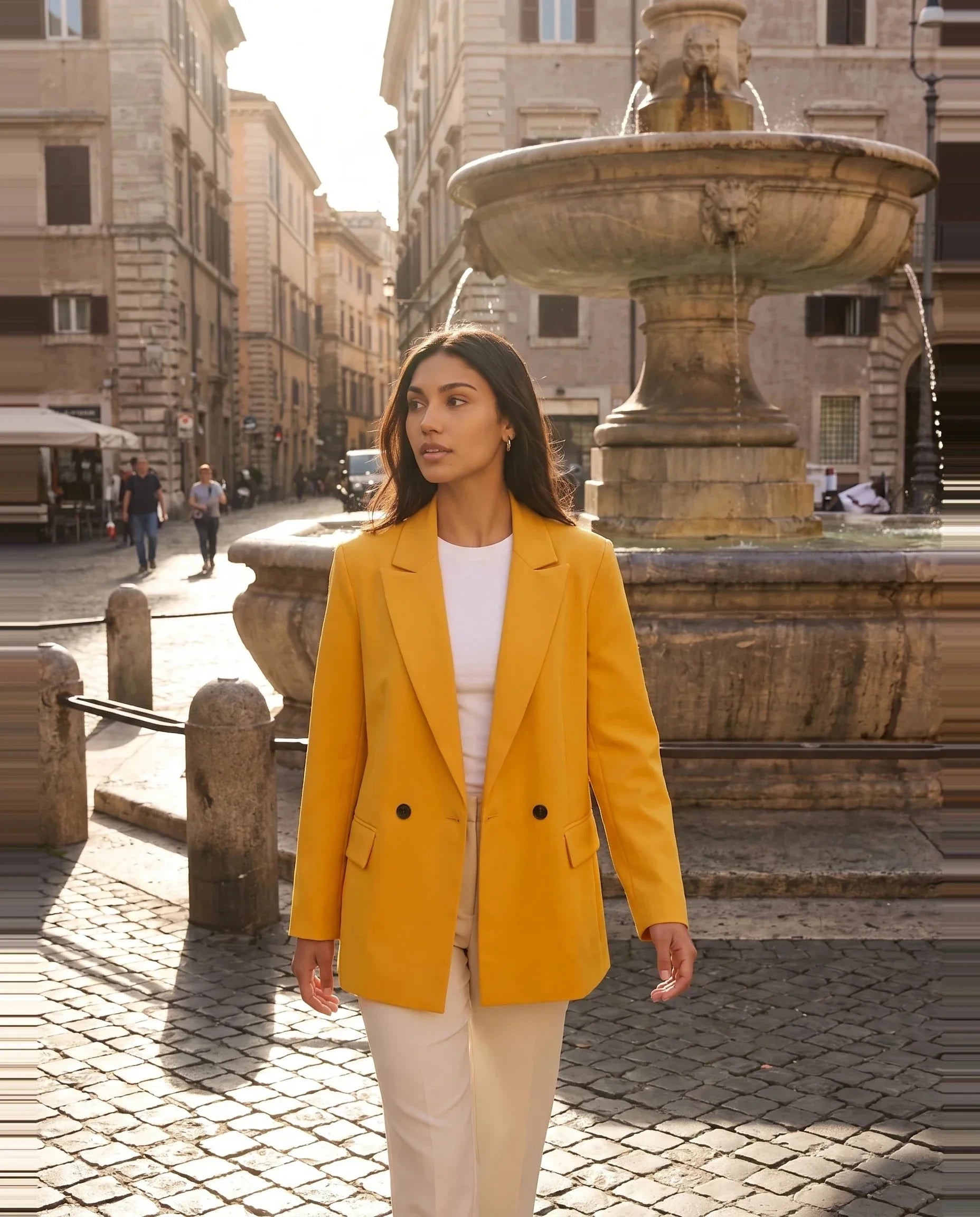 Blazer jaune safran Cosima, porté sur une place ensoleillée à la fontaine de pierre