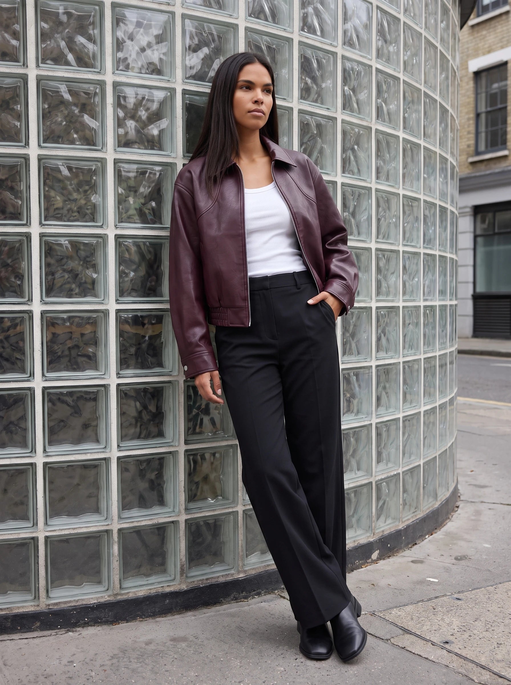 Blouson moto effet cuir lie de vin Marcelle, porté devant un mur de briques de verre