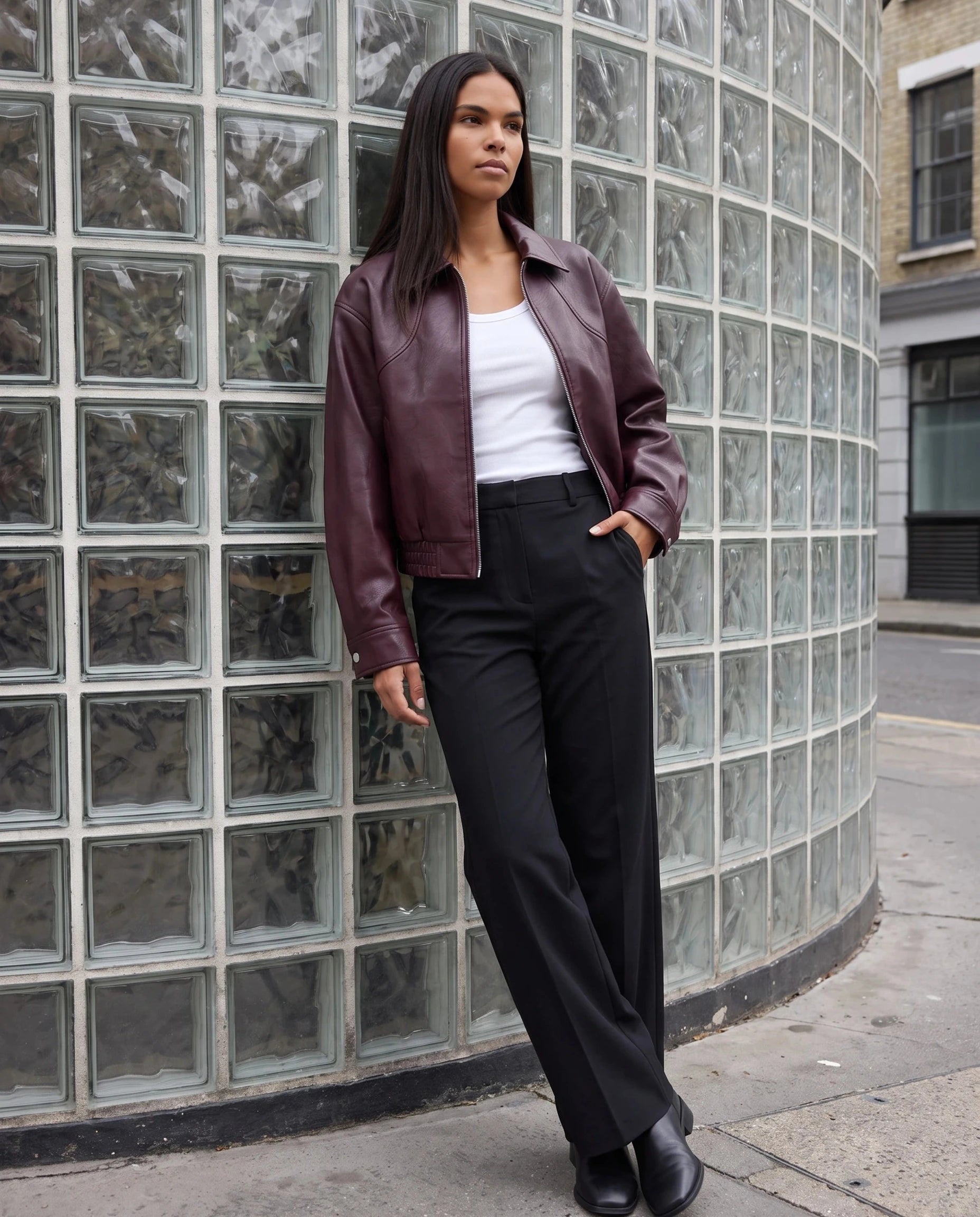 Blouson moto effet cuir lie de vin Marcelle, porté devant un mur de briques de verre