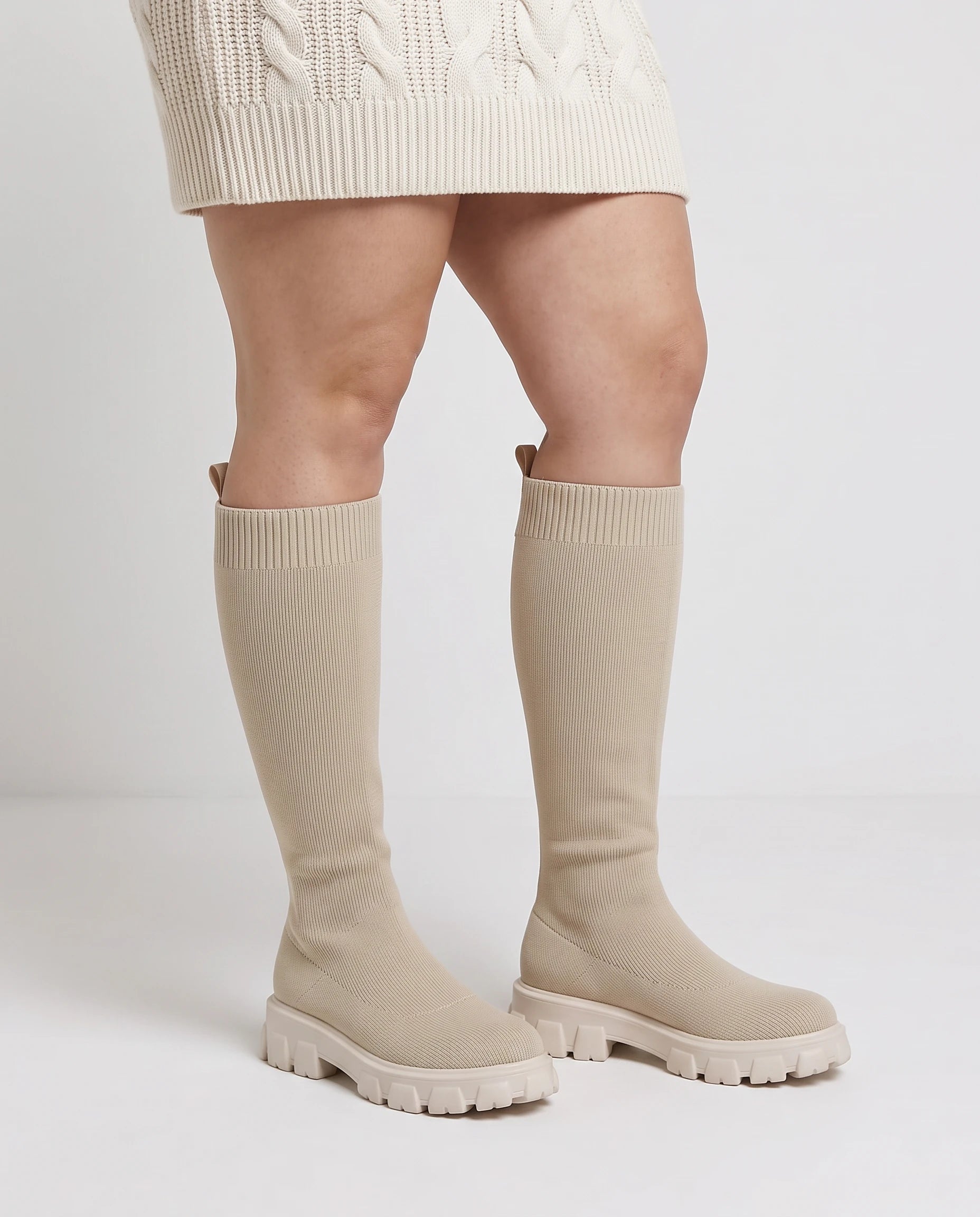 Bottes chaussettes hautes en maille Sylvette — Beige, portées en plan rapproché avec une robe pull écrue