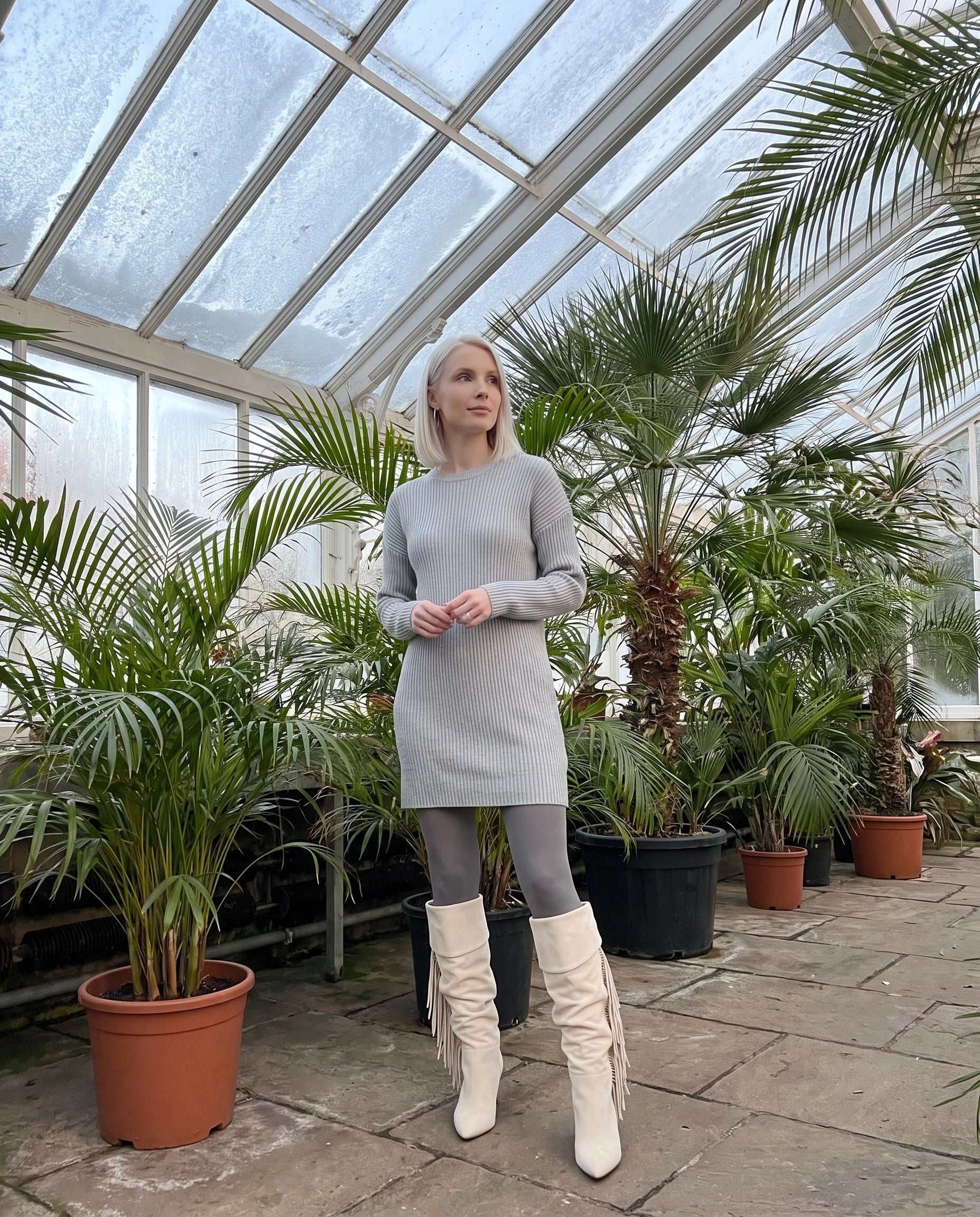 Bottes hautes à franges à talon compensé Alexandrine — Blanc Cassé, portées dans un jardin d'hiver sous verrière