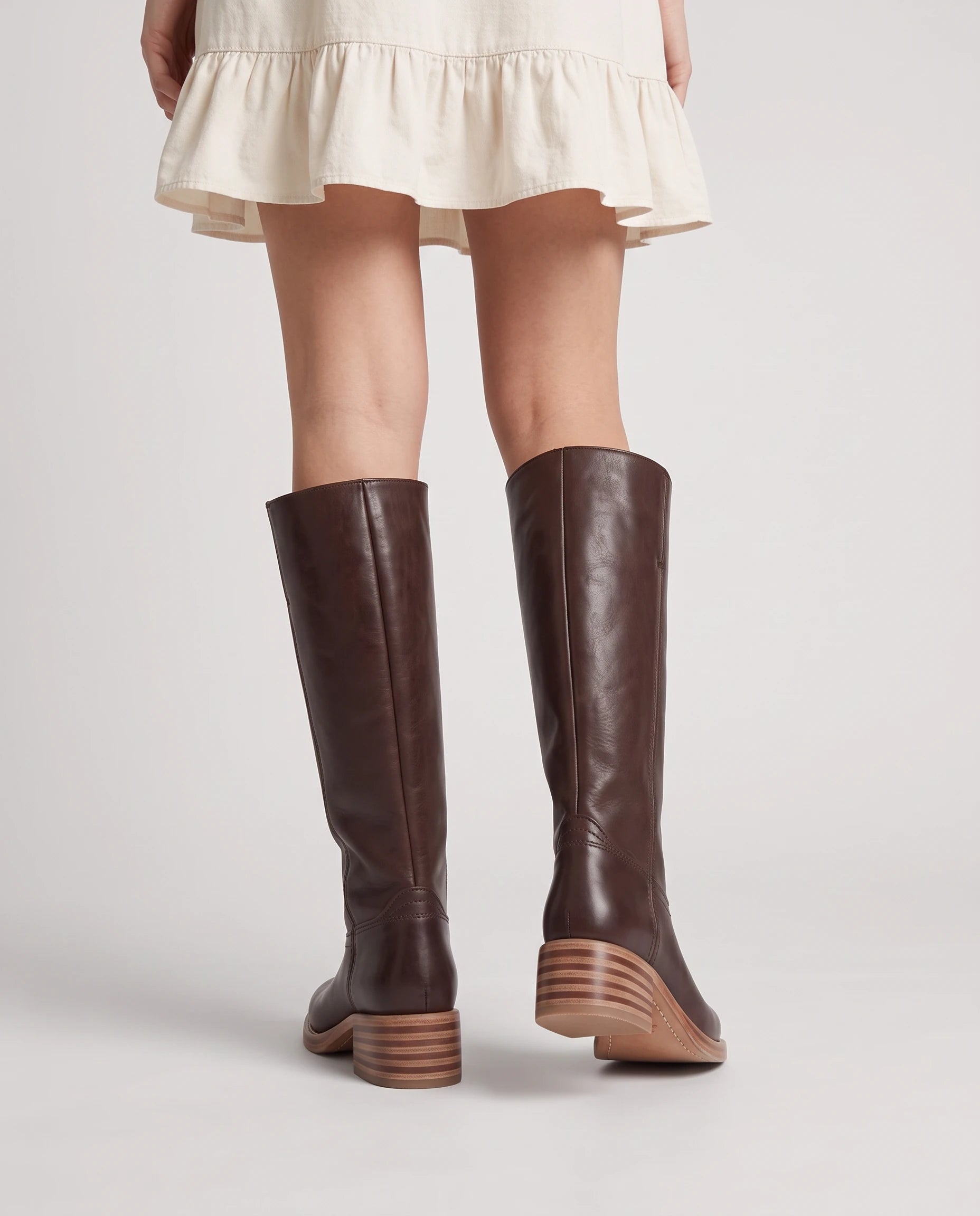 Bottes hautes à talon empilé effet cuir Nicolette — Chocolat, portées en plan rapproché vues de dos avec une robe courte
