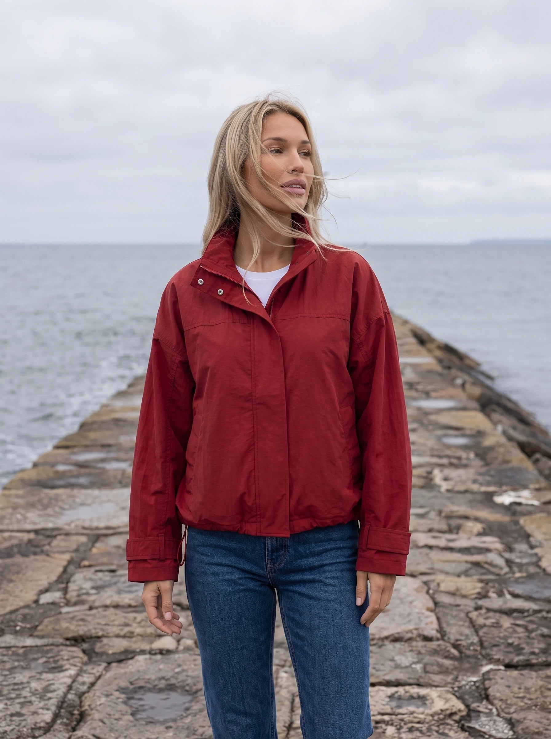 Coupe-vent rouge Ursule, porté sur une jetée de pierre face à la mer