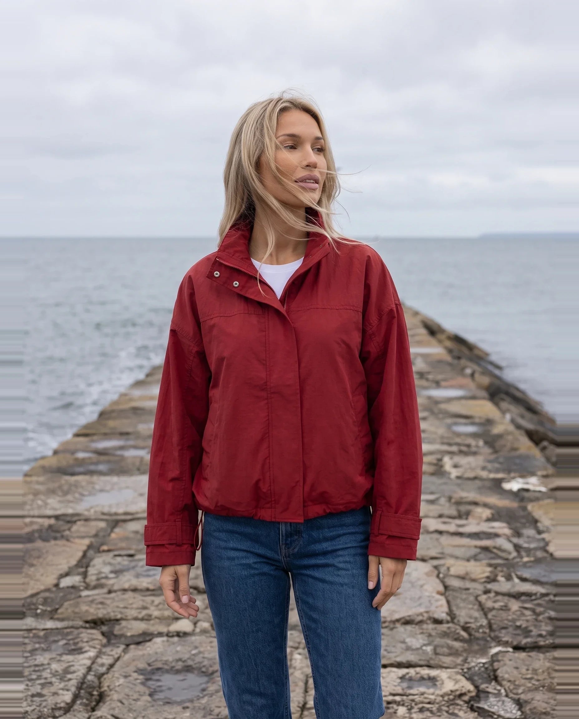 Coupe-vent rouge Ursule, porté sur une jetée de pierre face à la mer