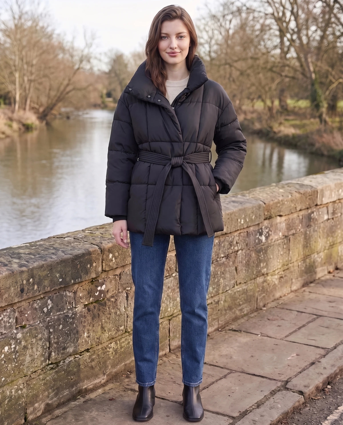 Steppjacke mit Bindegürtel und Stehkragen Lou in Schwarz, getragen auf einer Steinbrücke