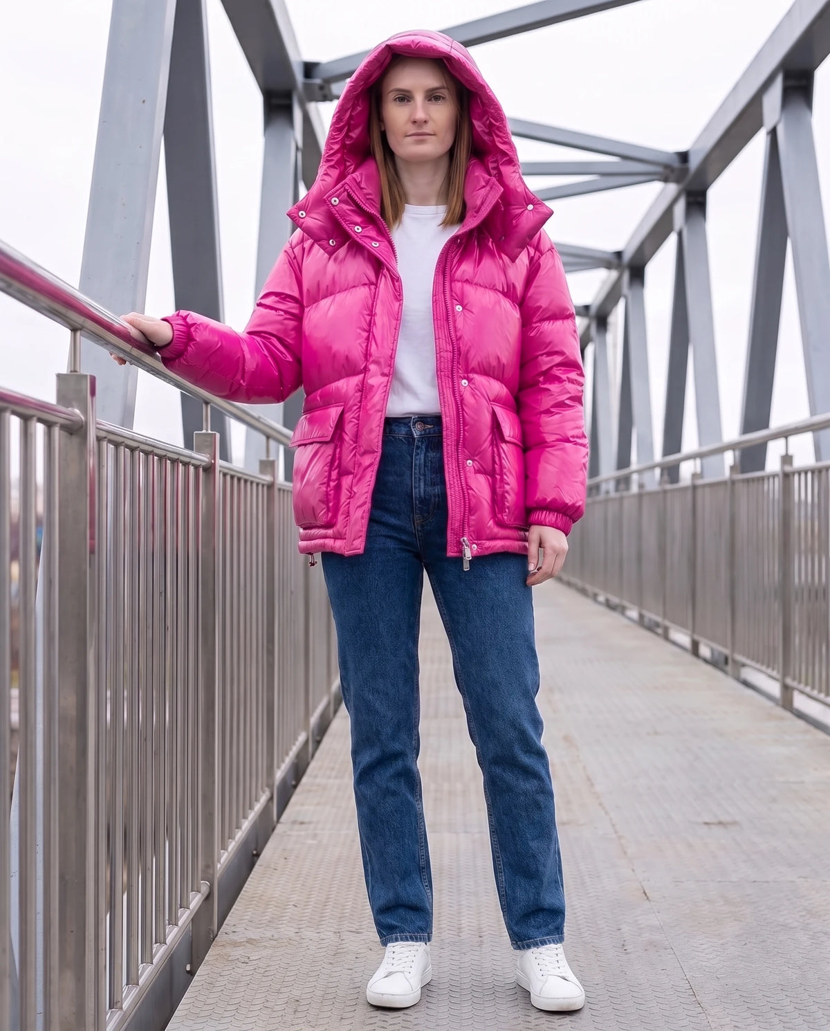 Doudoune courte brillante à capuche et poches plaquées Saskia en Fuchsia, portée sur une passerelle métallique, capuche relevée