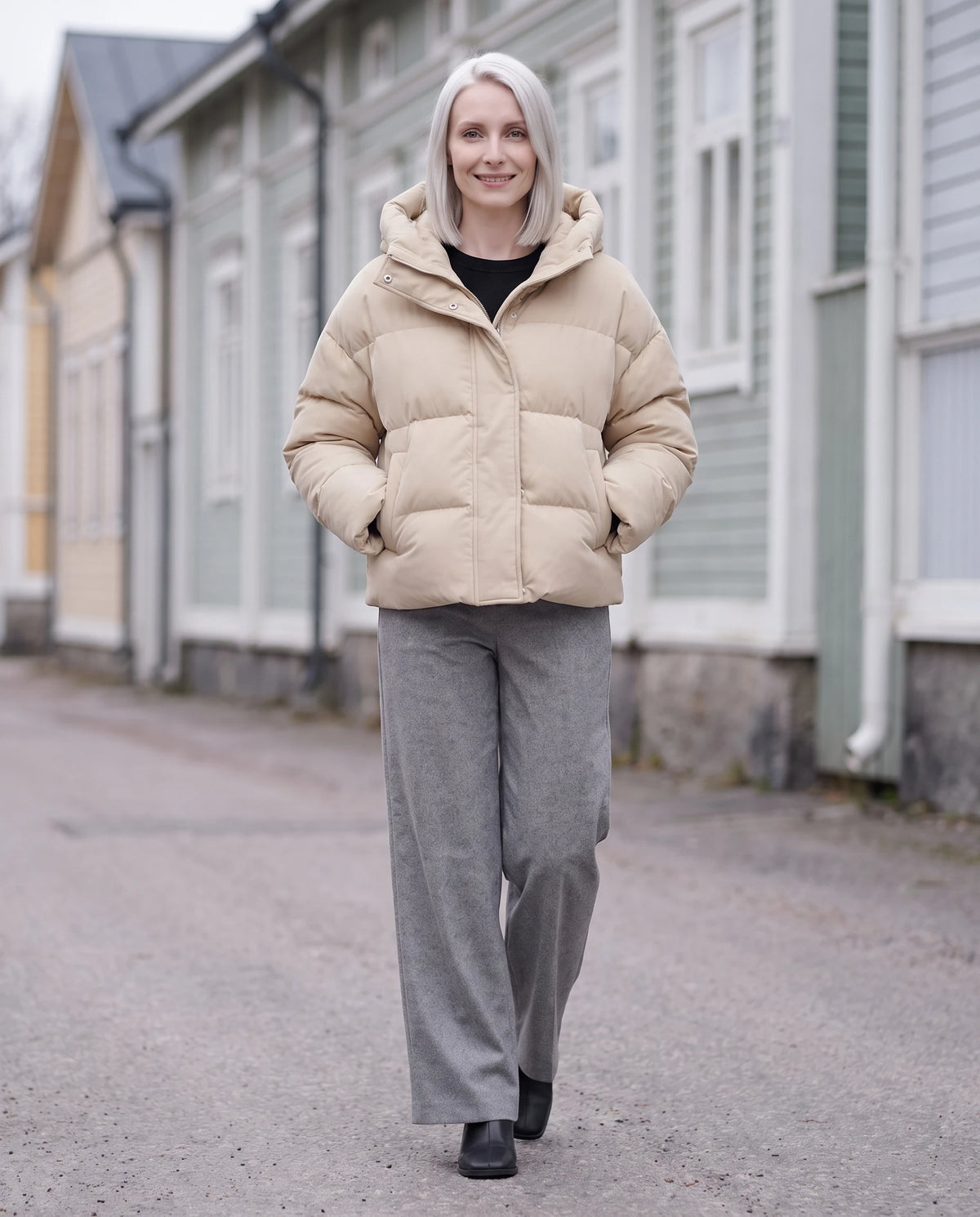Doudoune courte cropped en velours à capuche Carine en Avoine, portée dans une rue bordée de maisons de bois