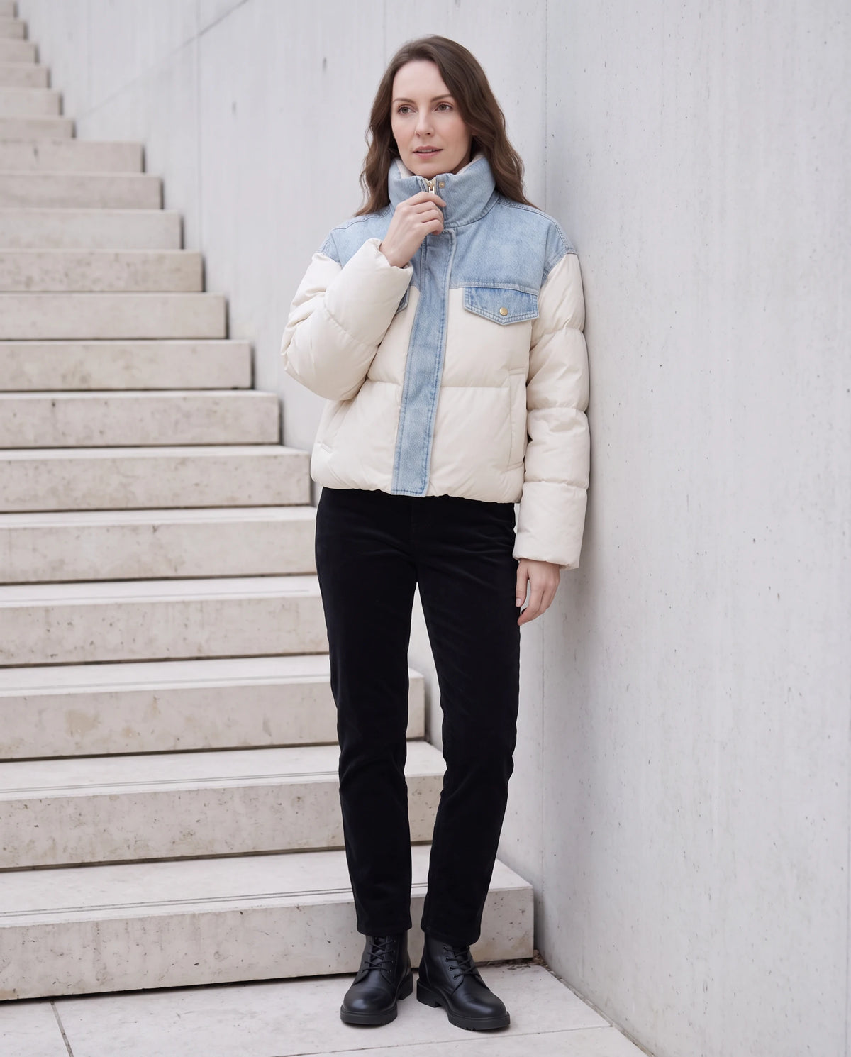 Doudoune courte oversize à empiècements en denim Annabelle écru, adossée à un mur de béton clair près d'un escalier