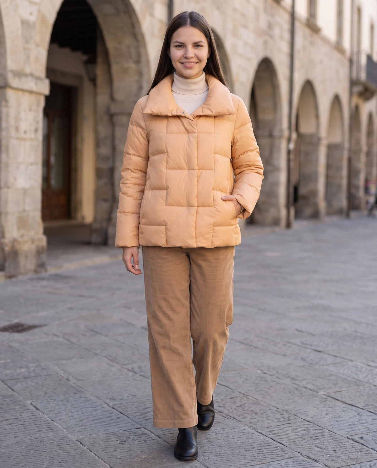 Kurze Steppjacke mit grossem Kragen und grossen Karos Stéphanie in Apricot, getragen auf einem Platz mit Arkaden