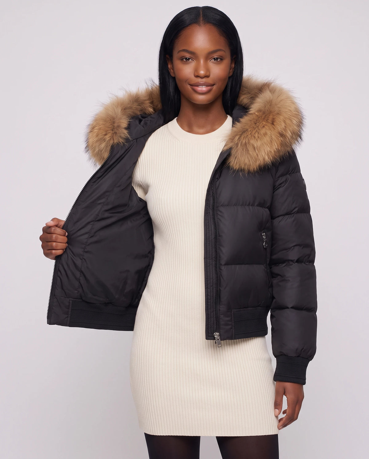 Kurze Steppjacke mit grosser Kunstfellkapuze Rebecca in Schwarz · naturfarbenes Fell, offen getragen über cremefarbenem Strickkleid