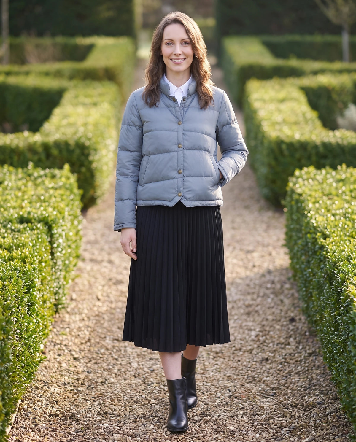 Doudoune courte légère façon blouson à pressions Christelle en Bleu Gris, portée sur une allée de gravier bordée de buis