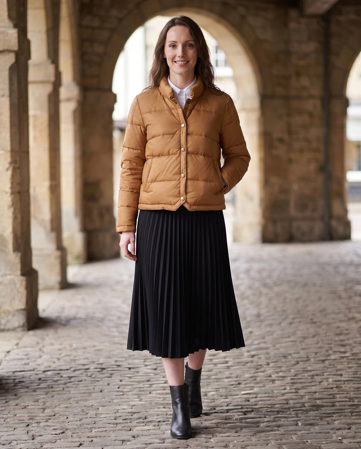 Doudoune courte légère façon blouson à pressions Christelle en Caramel, portée sous les arcades d'une halle de pierre