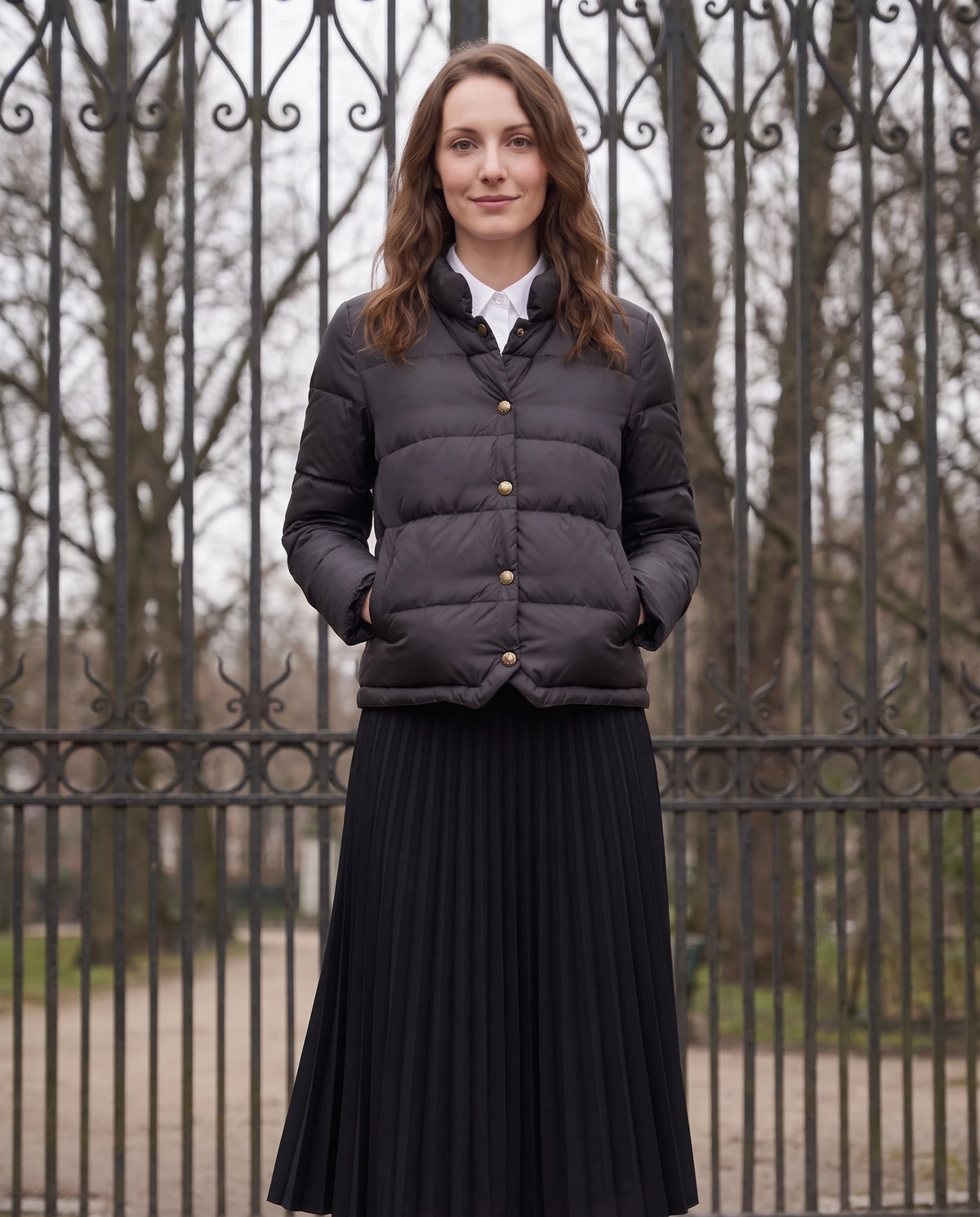 Doudoune courte légère façon blouson à pressions Christelle en Noir, portée devant une grille de parc en fer forgé