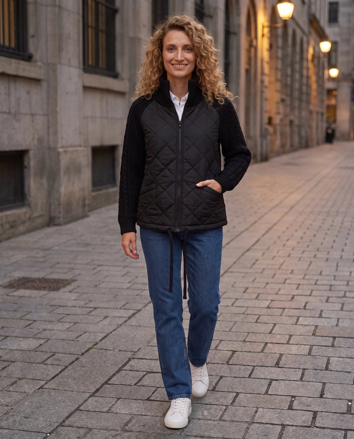 Doudoune courte à manches tricot Emma en Noir, portée sur un trottoir urbain au crépuscule