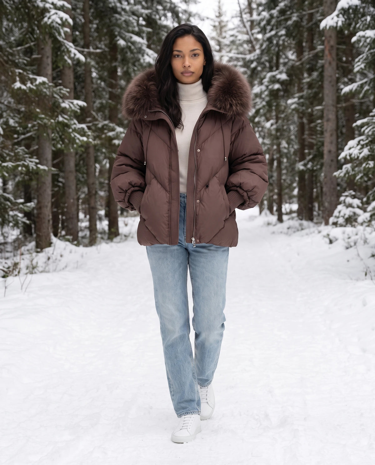 Doudoune courte oversize à capuche fausse fourrure Anna en Marron, portée sur un chemin forestier enneigé