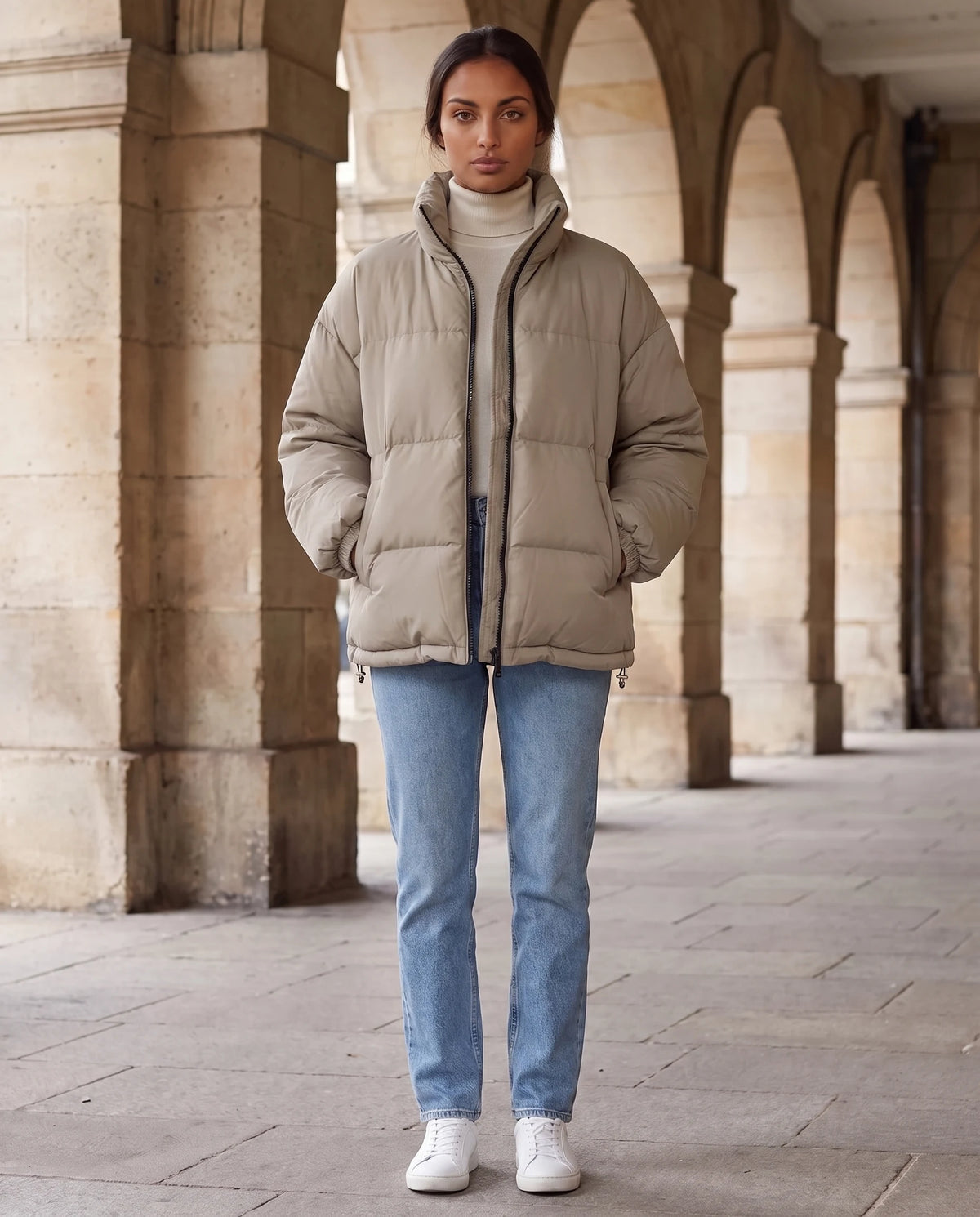 Doudoune courte oversize col montant zip contrasté Alice en Grège, portée sous des arcades de pierre, cordon d'ourlet serré