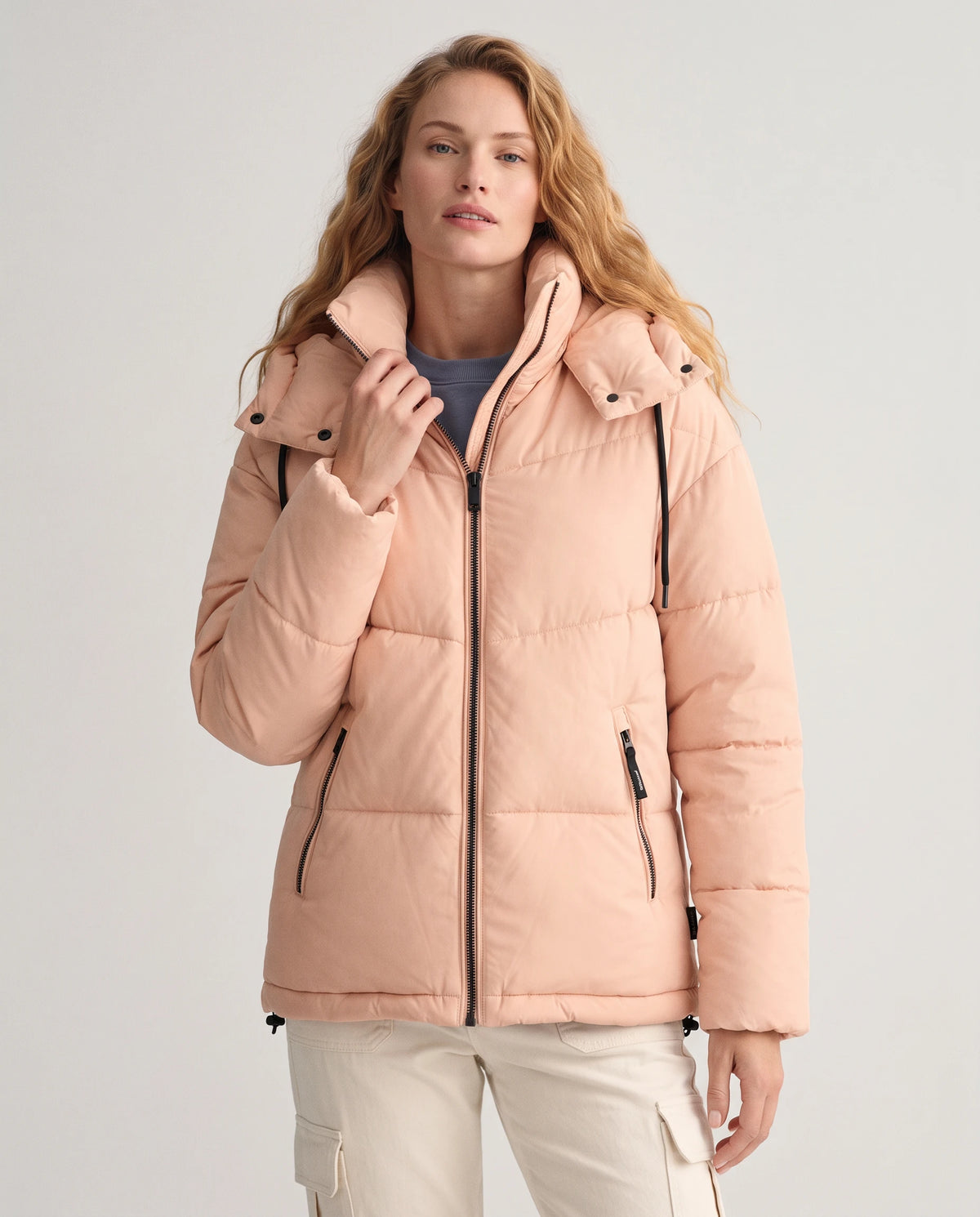 Doudoune courte oversize à capuche Lubine en Rose Pêche, plan rapproché, main qui ajuste le col montant
