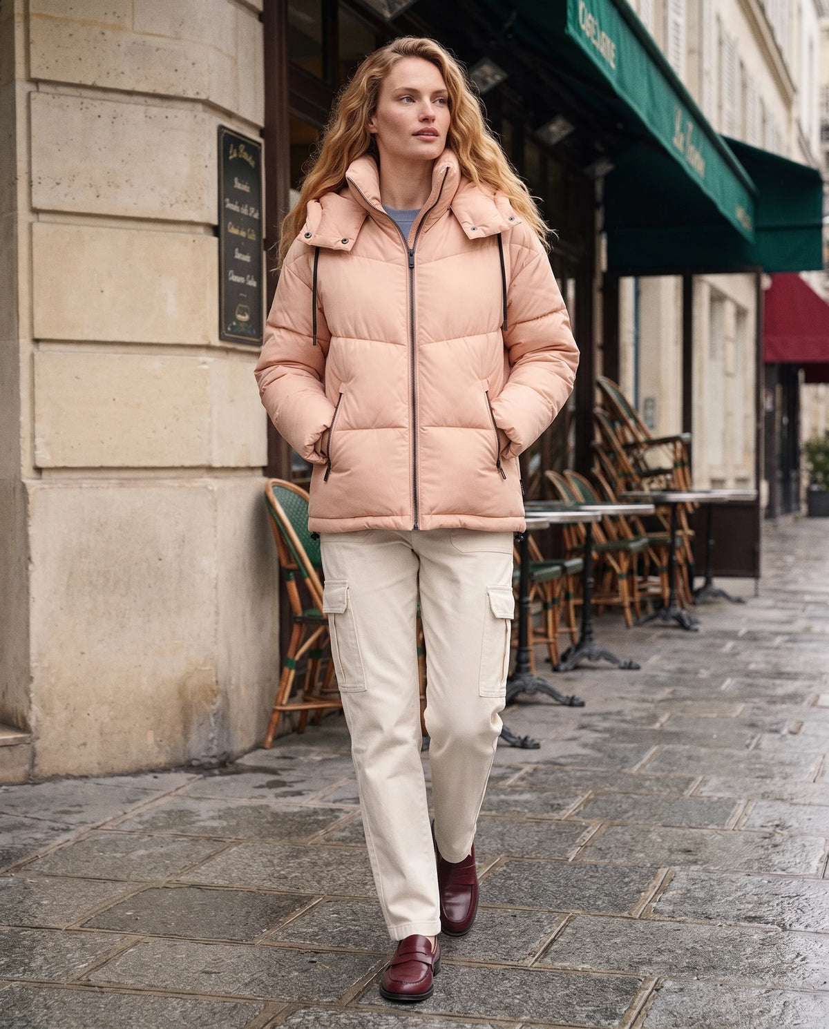 Doudoune courte oversize à capuche Lubine en Rose Pêche, portée en rue devant une façade en pierre claire