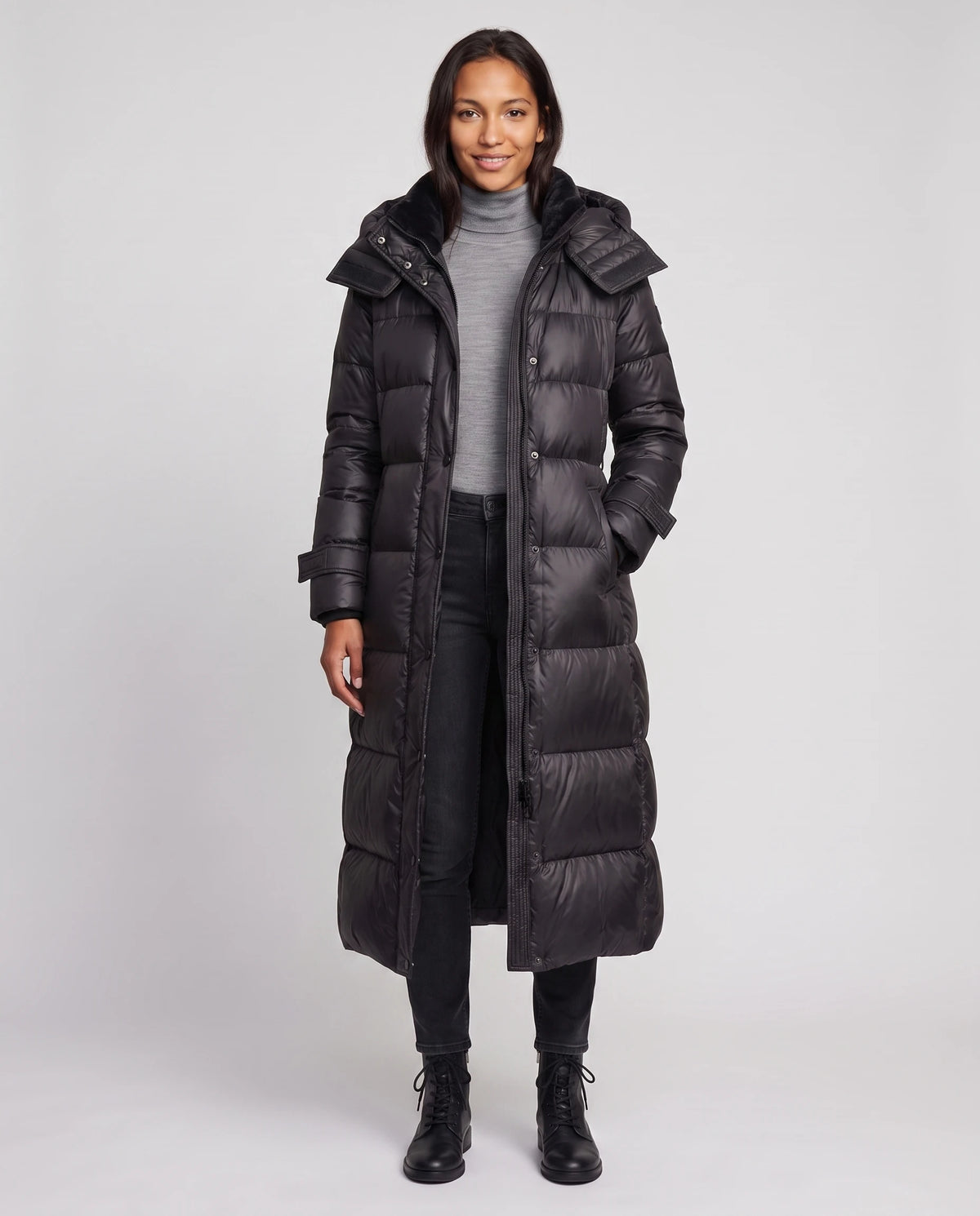 Extralange glänzende Steppjacke mit Kapuze und Schnallengürtel Carole in Schwarz, offen getragen ohne Gürtel über grauem Rollkragen