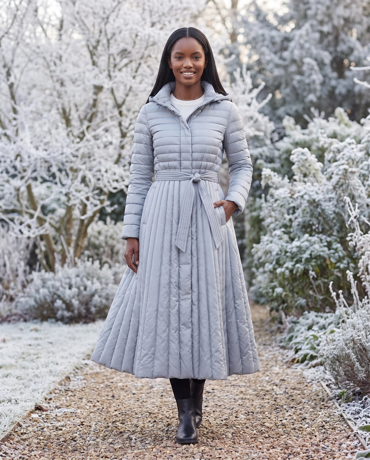 Doudoune extra-longue évasée à capuche et ceinture Tatiana en Gris Argenté, portée dans un jardin d'hiver aux arbres givrés