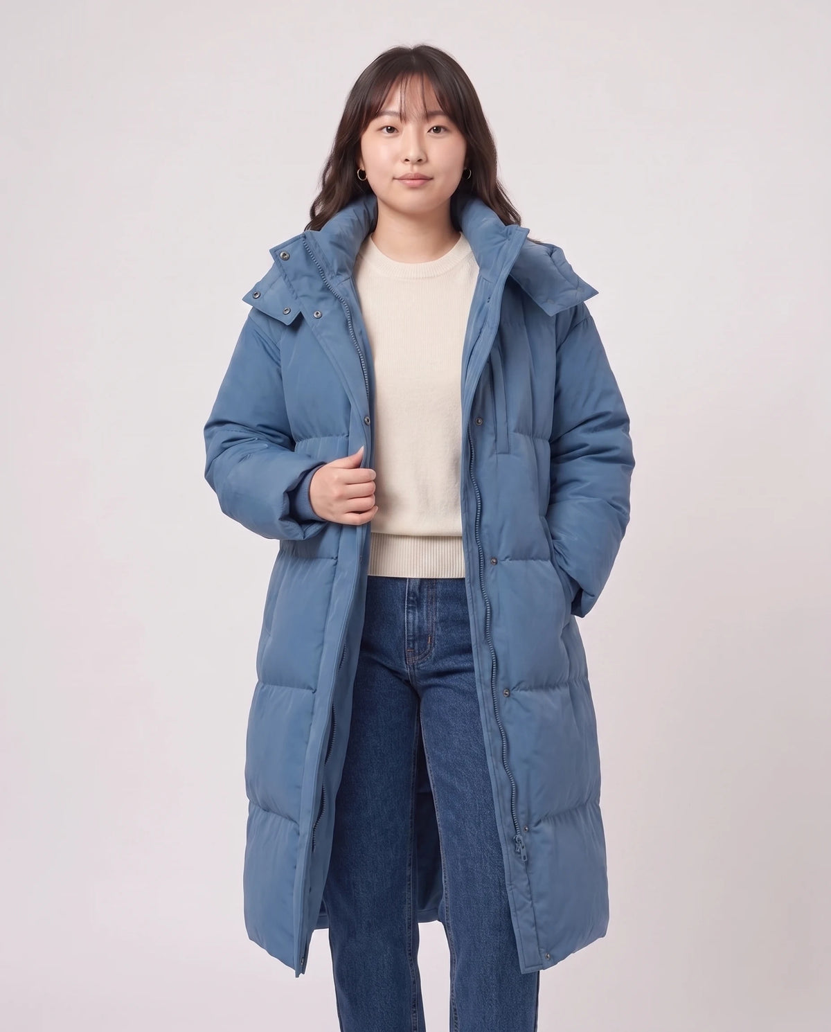 Langer Oversize-Steppmantel mit Kapuze Enora in Denimblau, offen getragen über ecrufarbenem Pullover, Futter sichtbar