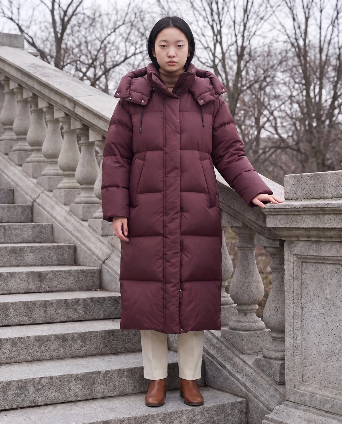 Doudoune maxi oversize à capuche et pressions Marine en Bordeaux, portée sur un escalier extérieur en pierre grise