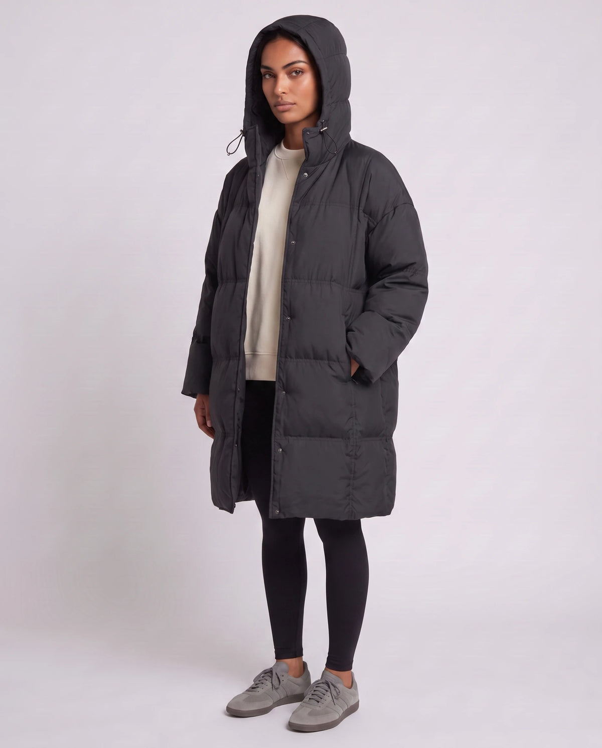 Doudoune mi-longue oversize à capuche cordon et pressions cachées Emmanuelle en Noir, vue de trois quarts, capuche relevée, mains dans les poches