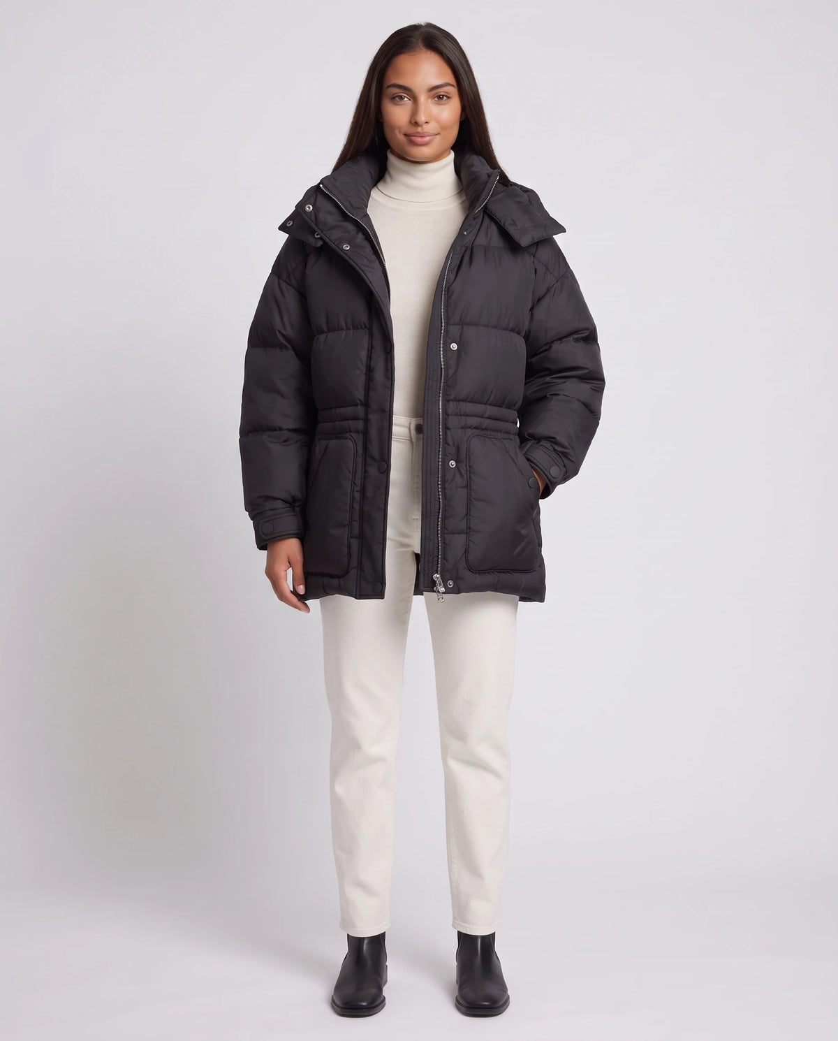 Doudoune oversize mi-cuisse à capuche et ceinture à boucle Sophia en Noir, portée ouverte sans ceinture sur un col roulé crème