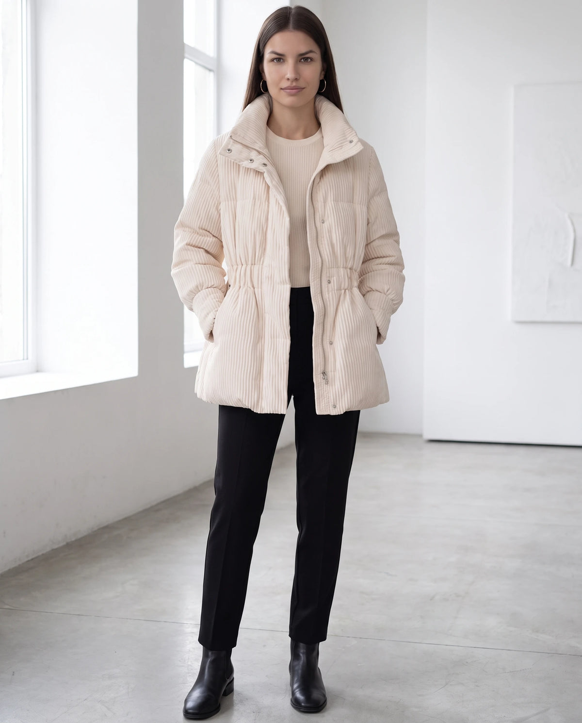 Halblange Plissee-Steppjacke Ilaria in Beige, getragen in einer minimalistischen Galerie