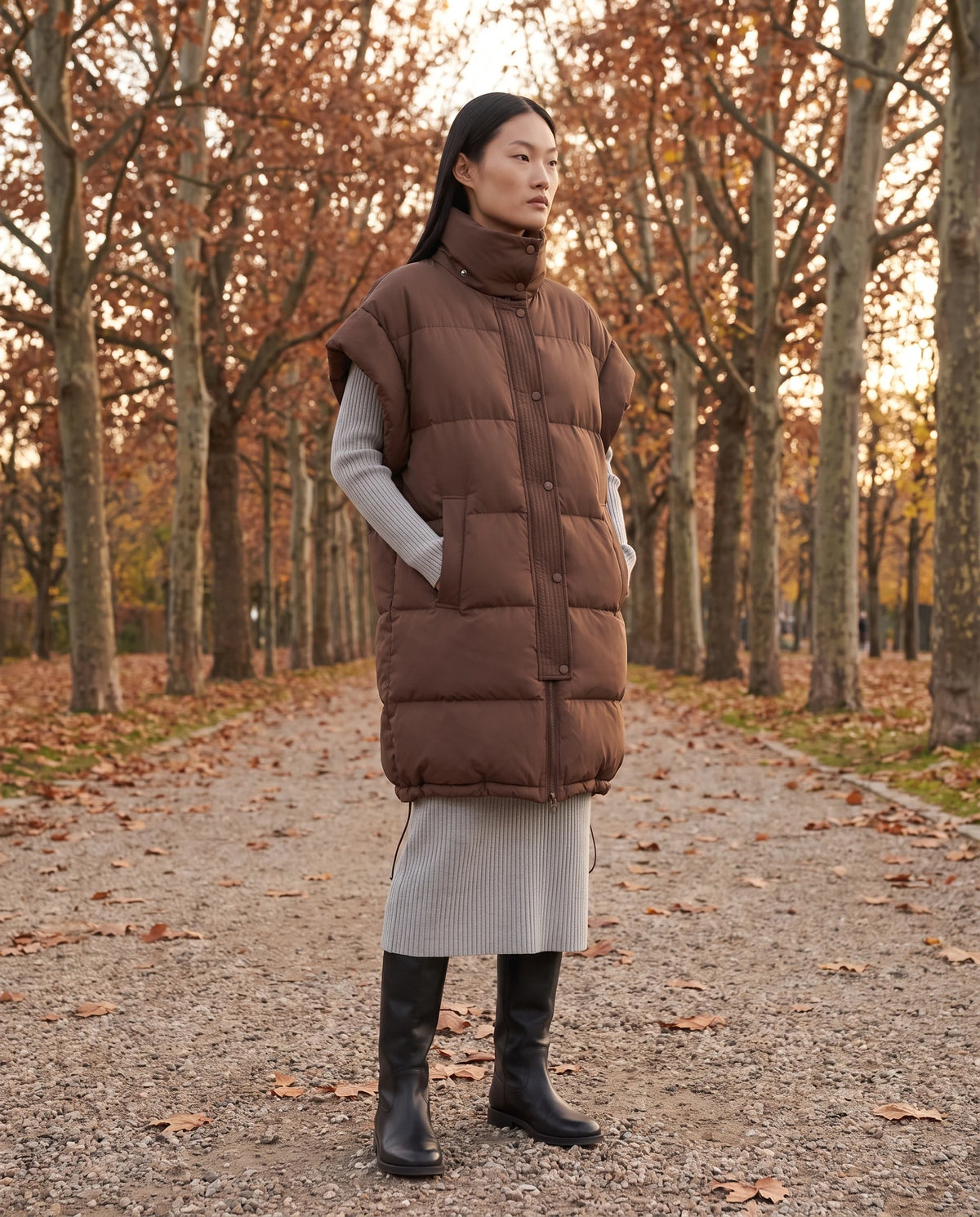 Doudoune sans manches oversize à grand col et patte plissée Perline en Chocolat, portée dans une allée de platanes aux feuilles rousses