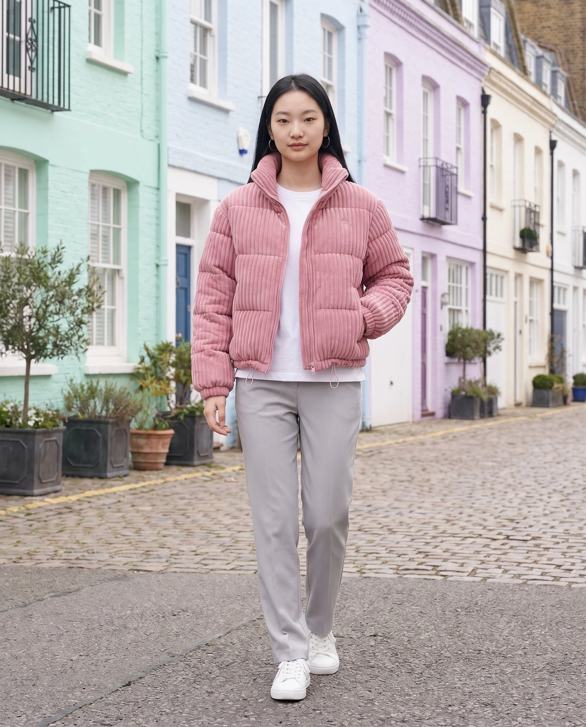 Doudoune courte en velours côtelé Lucia en Rose, portée dans une rue de maisons pastel