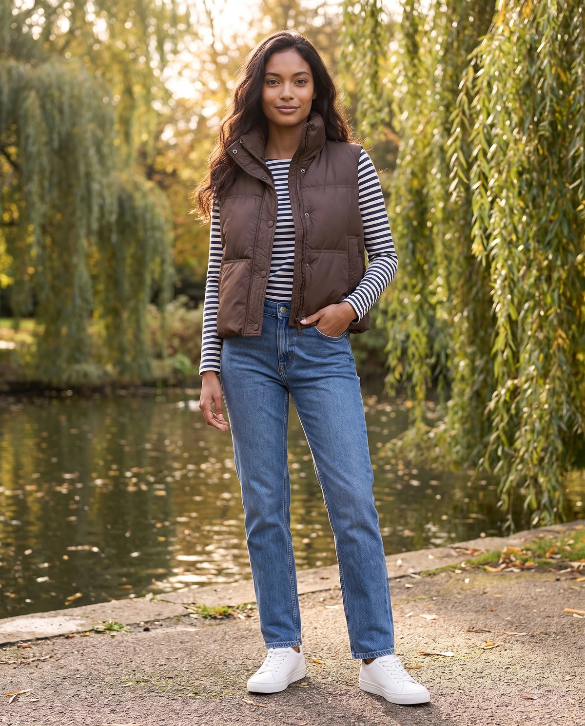 Gilet matelassé cropped à col montant et patte à pressions Soline en Marron, portée dans un parc au bord d'un étang aux saules
