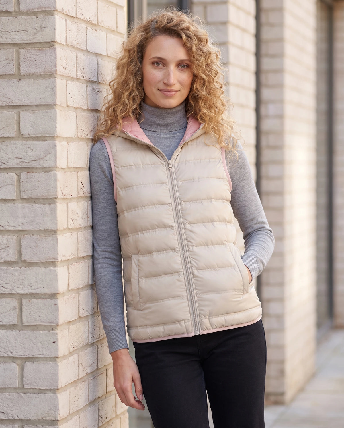 Gilet matelassé léger à capuche et doublure contrastée Laurence en Beige, portée contre un mur de brique claire