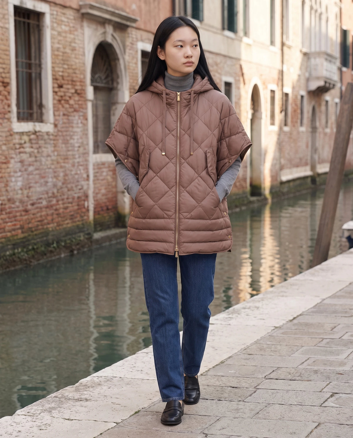 Gilet matelassé à capuche et pressions Céline en Brun Cacao, portée dans une rue calme le long d'un canal aux façades de brique