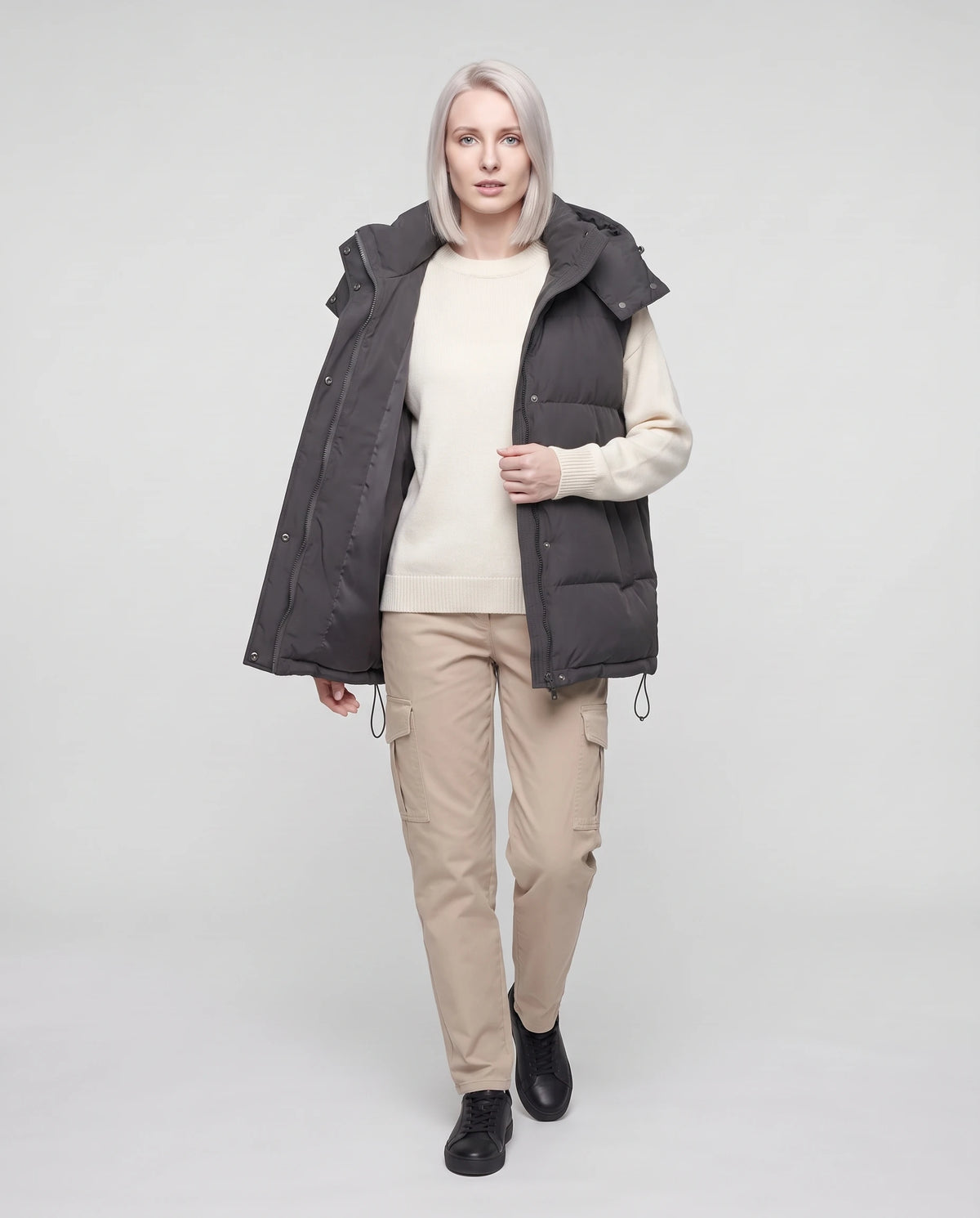 Gilet matelassé oversize à capuche amovible Patricia en Gris Anthracite, porté ouvert sur un sweat écru, cordon d’ourlet relâché