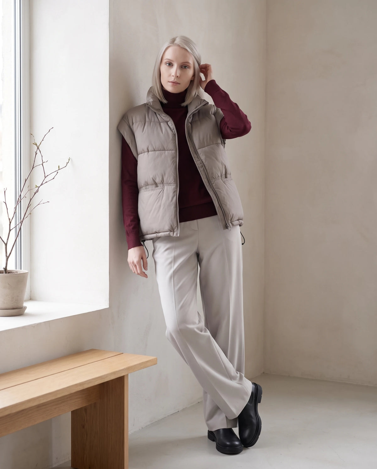 Gilet matelassé sans manches à poches plaquées Anceline en Gris Taupe, porté dans un intérieur clair près d'une grande fenêtre