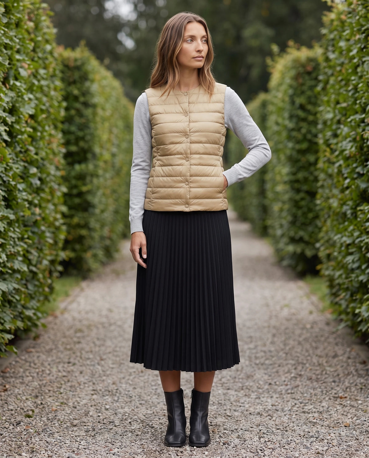 Gilet ultra-léger à col rond transformable Valérie en Beige Sable, porté sur une allée de gravier entre deux hautes haies