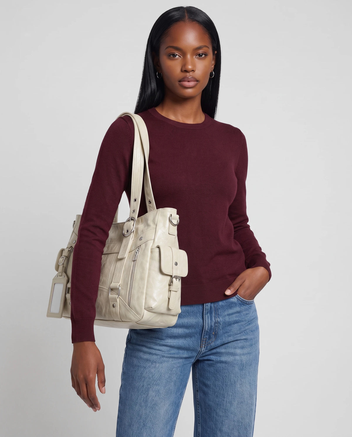 Grand sac à main cabas de cours style motard à boucles Pia coloris Crème, porté à l'épaule, calé sous le bras, sur un pull fin bordeaux