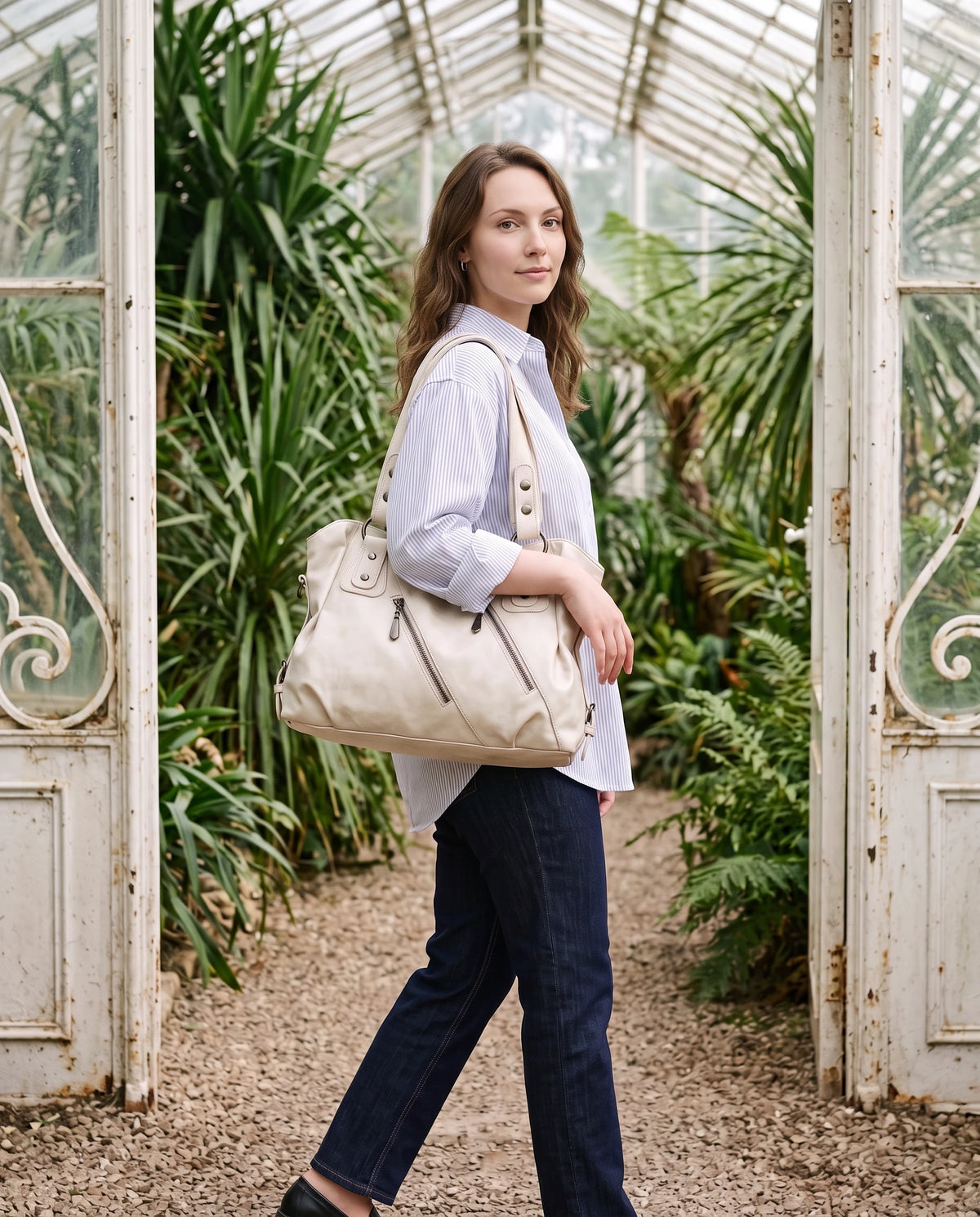 Grand sac à main hobo bandoulière style motard à zips Thelma coloris Blanc Cassé, porté à l'épaule dans une serre en fer forgé