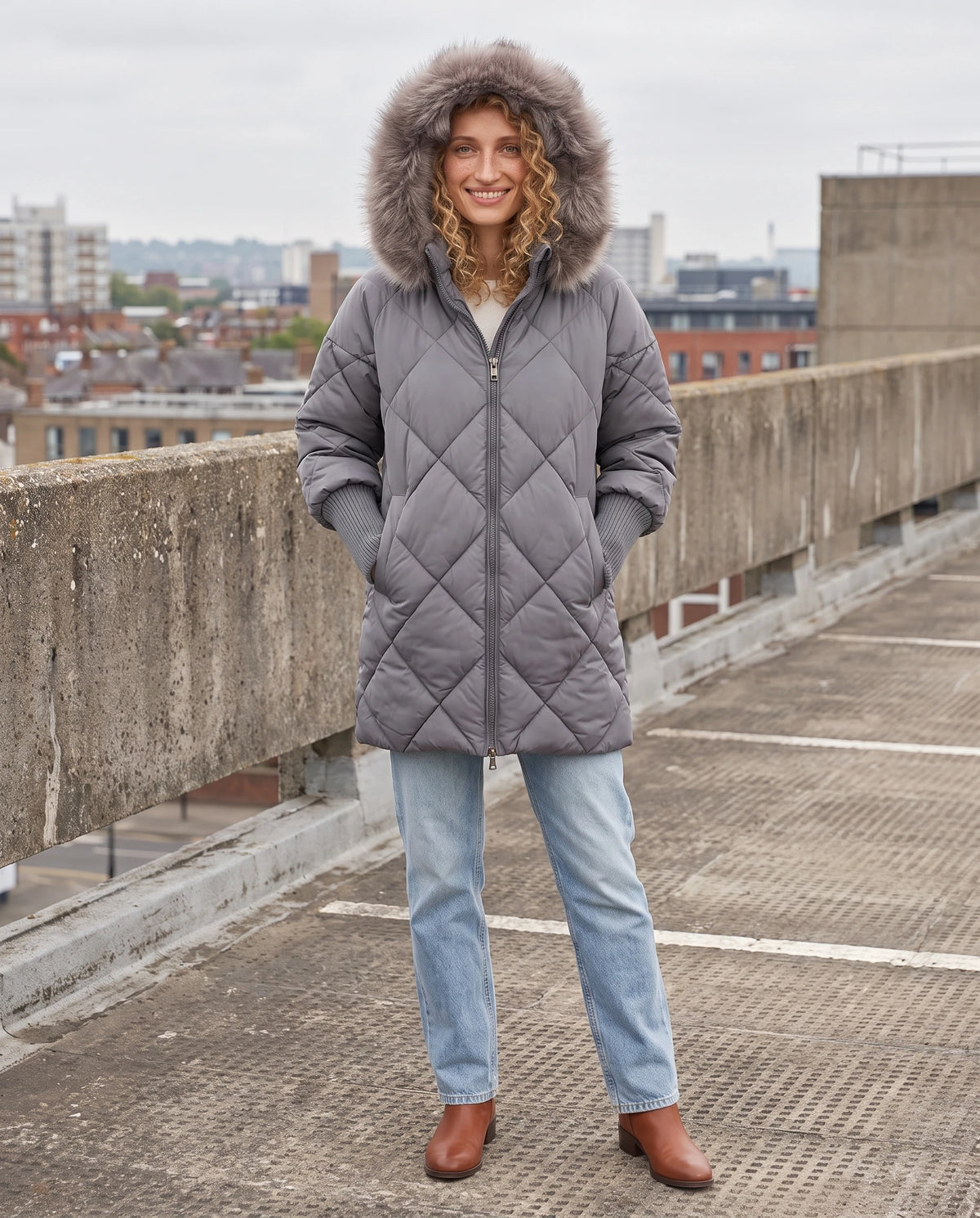 Parka mi-longue matelassée à manches tricot Ava en Gris, portée sur un parking à étages en béton, capuche relevée