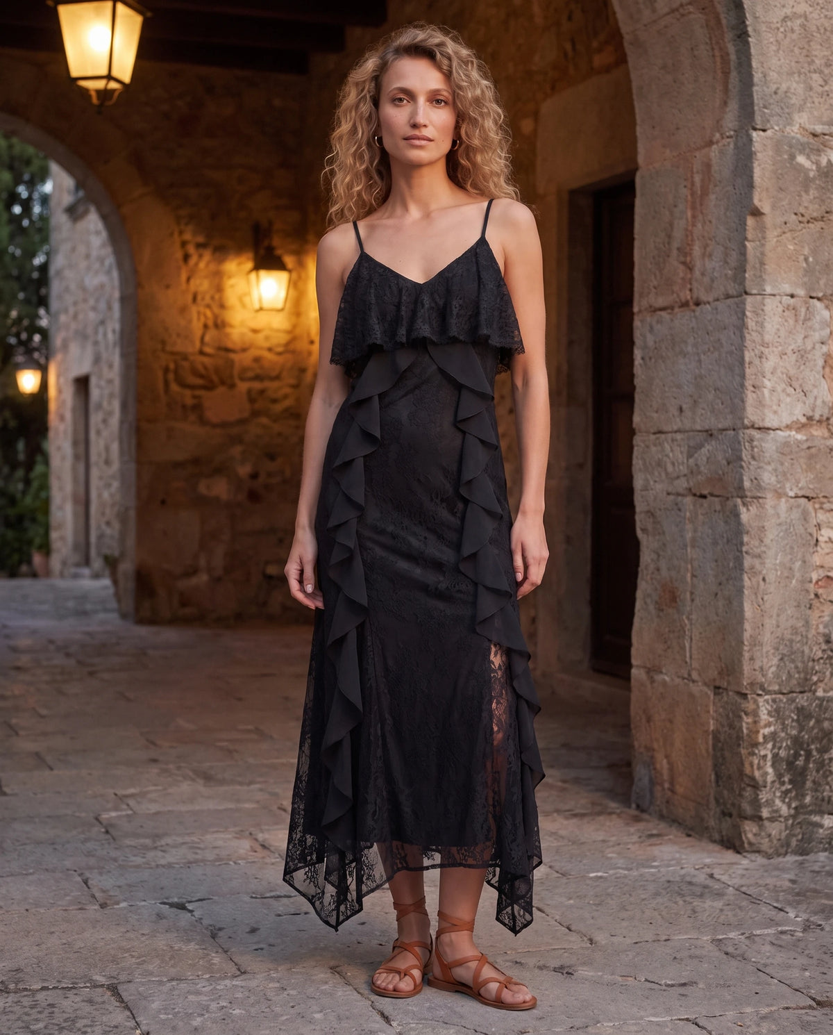 Langes Spitzenkleid mit Volants und Schlitz Amélia in Schwarz, unter einem Steinbogen in der Abenddämmerung getragen