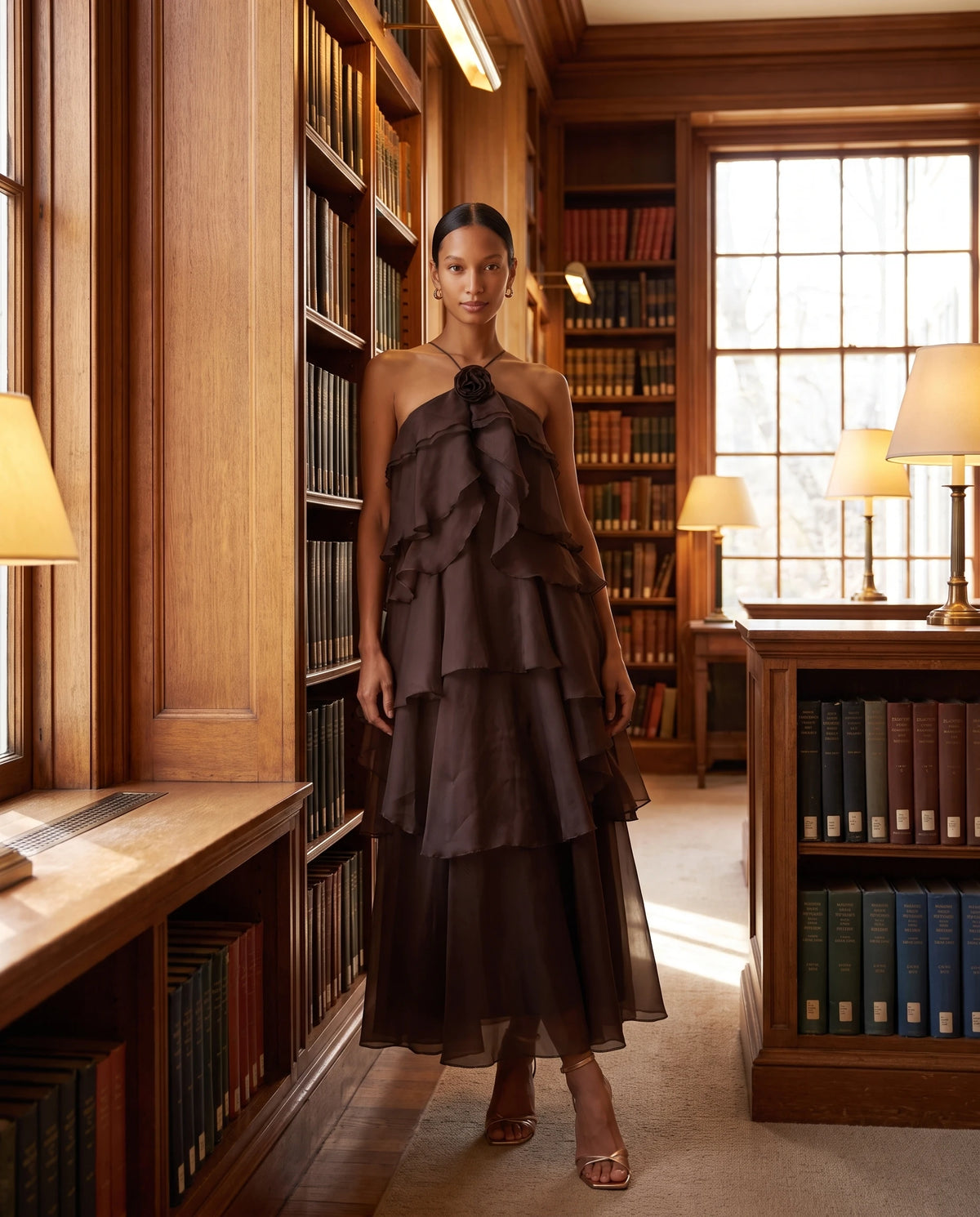 Robe longue halter en organza à volants étagés Iliana en Chocolat Foncé, portée dans une bibliothèque boisée