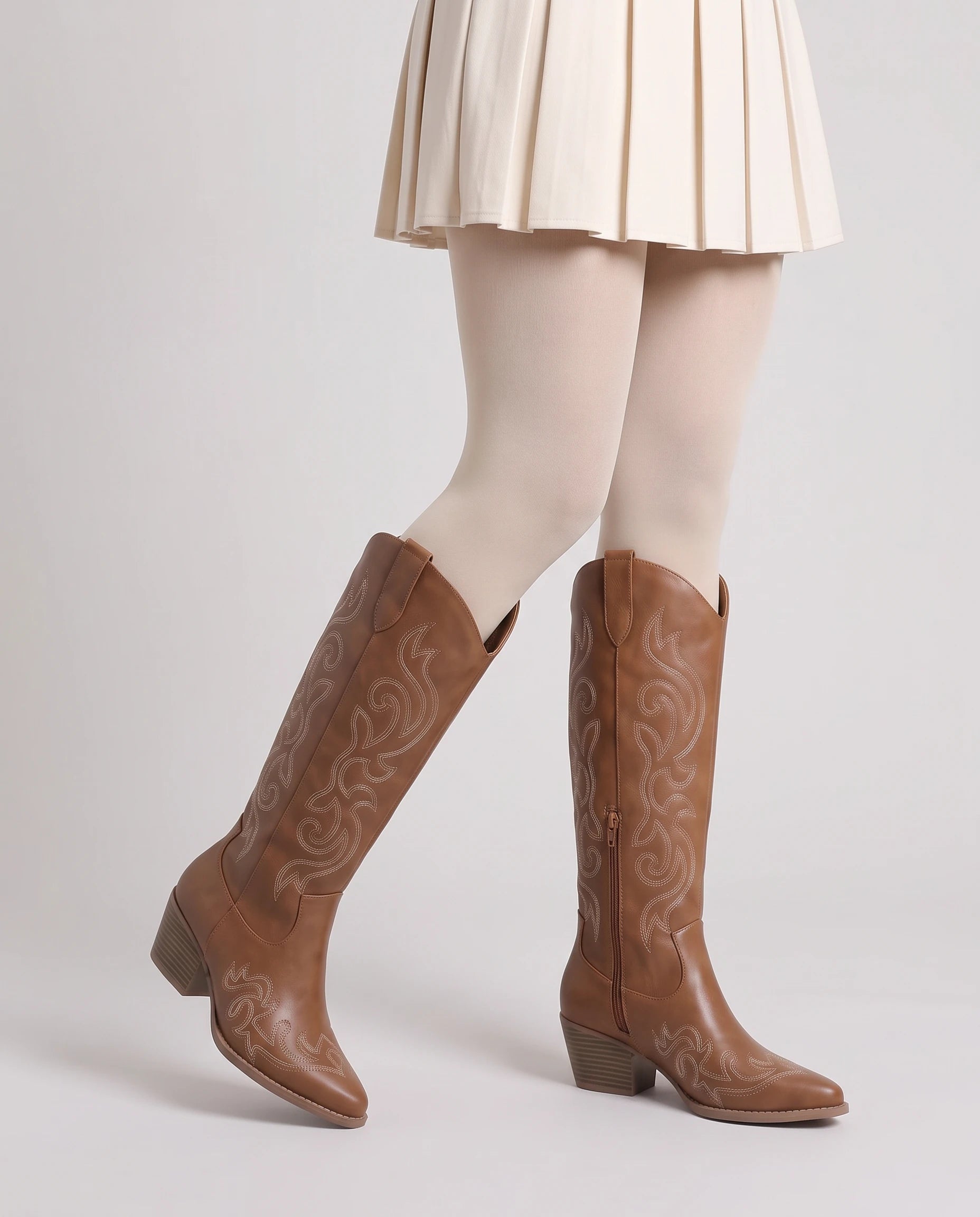 Bottes santiags hautes brodées Ghislaine — Noisette, portées en plan rapproché, un pied avancé