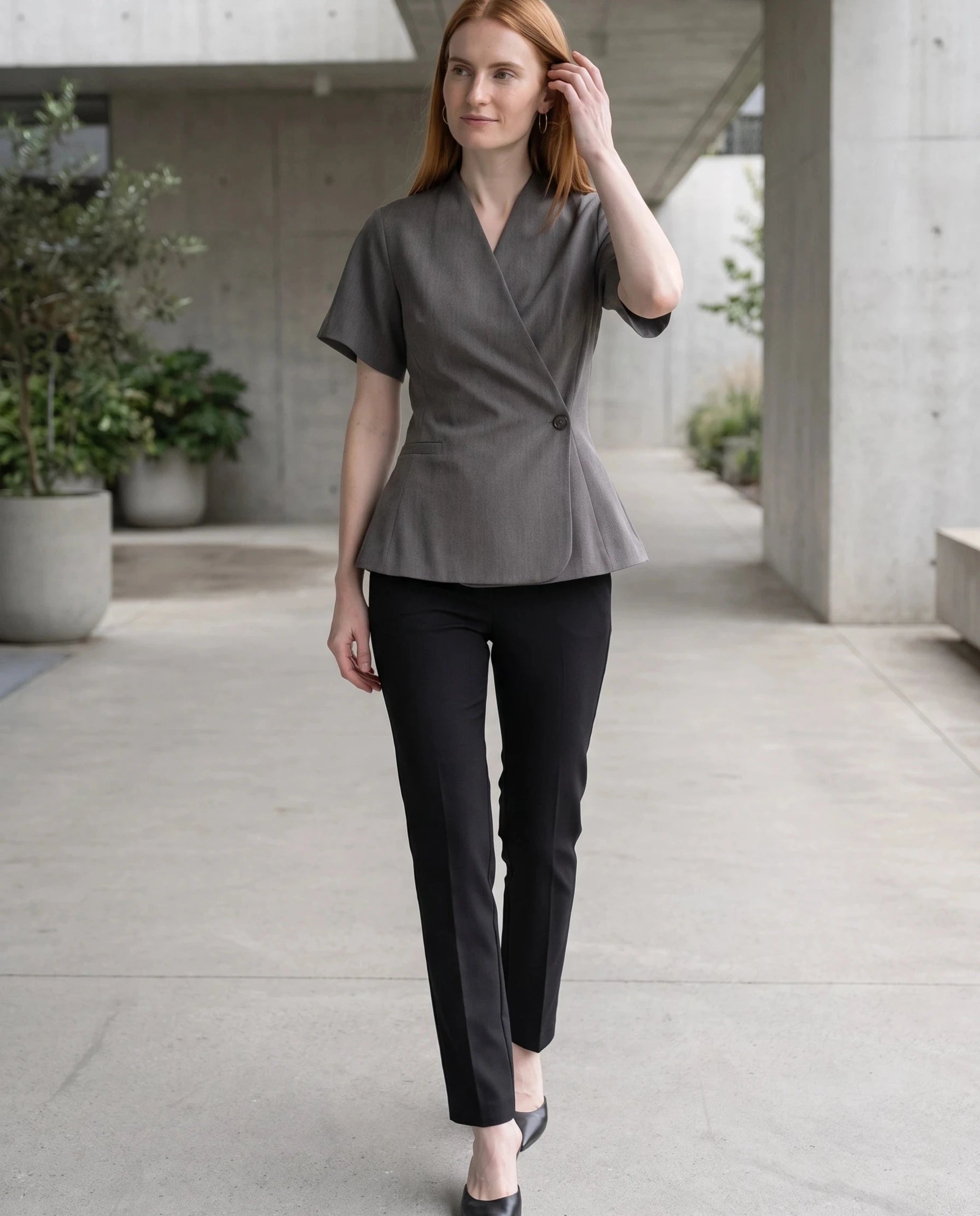 Veste cache-cœur gris chiné Célimène, portée dans un passage moderne en béton