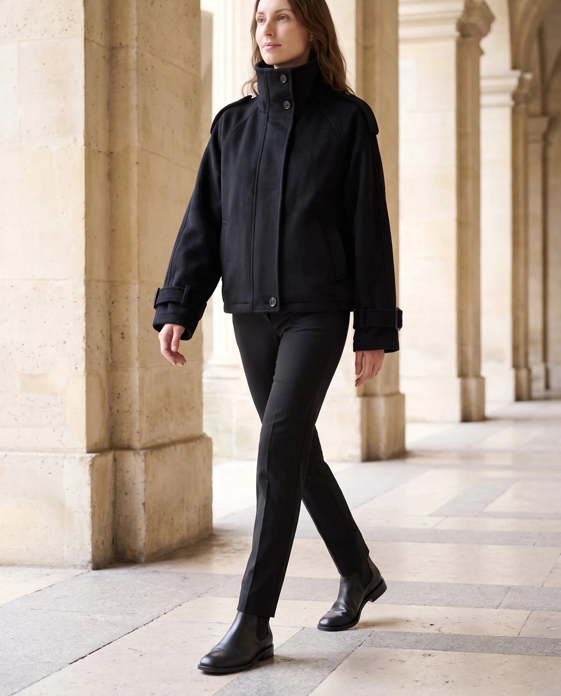 Veste cocon en lainage noir Josiane, portée le long d'une colonnade de pierre